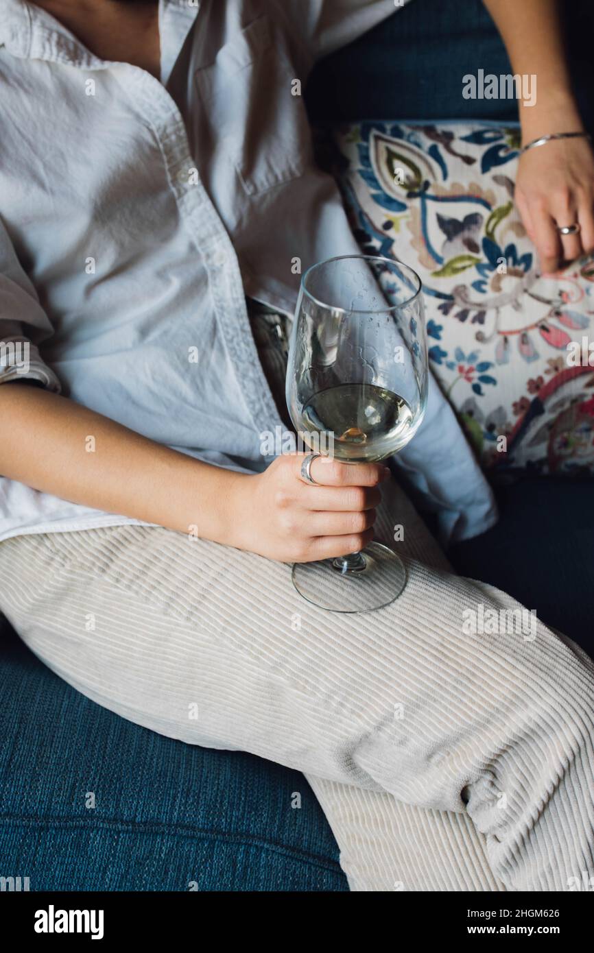 femme élégante et décontractée tenant un verre de vin blanc sur un canapé Banque D'Images