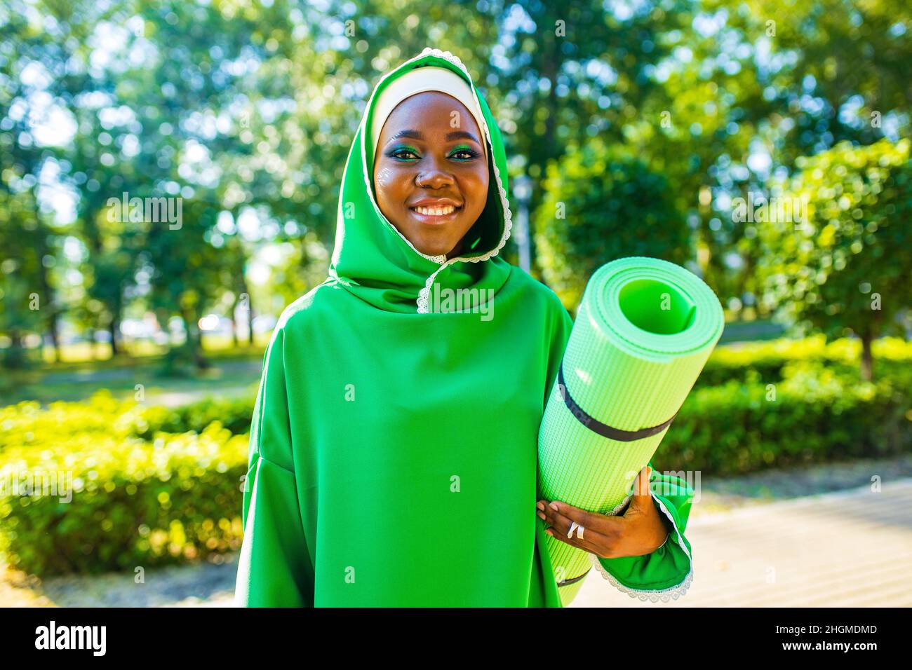 femme noire latine dans hijab vert avec maquillage lumineux et perçage nez holg tapis de yoga extérieur dans le parc d'été Banque D'Images