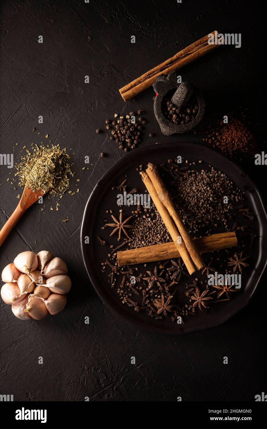 Sélection de différentes épices sur fond noir texturé.Poivre, cardamome, gousse, ail, cannelle,anis étoilé, persil déshydraté.Pose à plat Banque D'Images