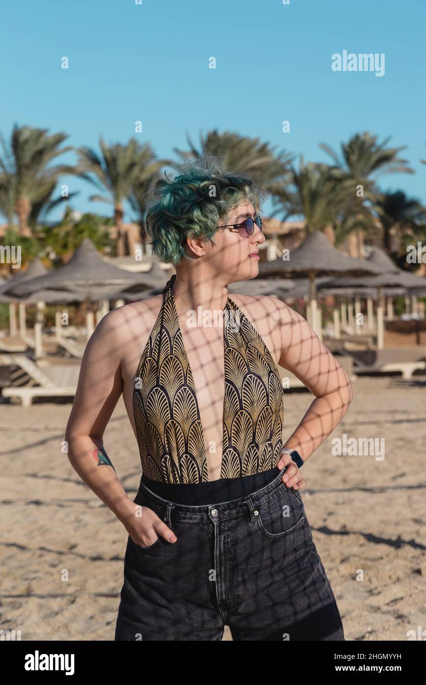 Jeune femme avec des cheveux bleus verts sur le sable de la plage à l'ombre de la grille. Banque D'Images