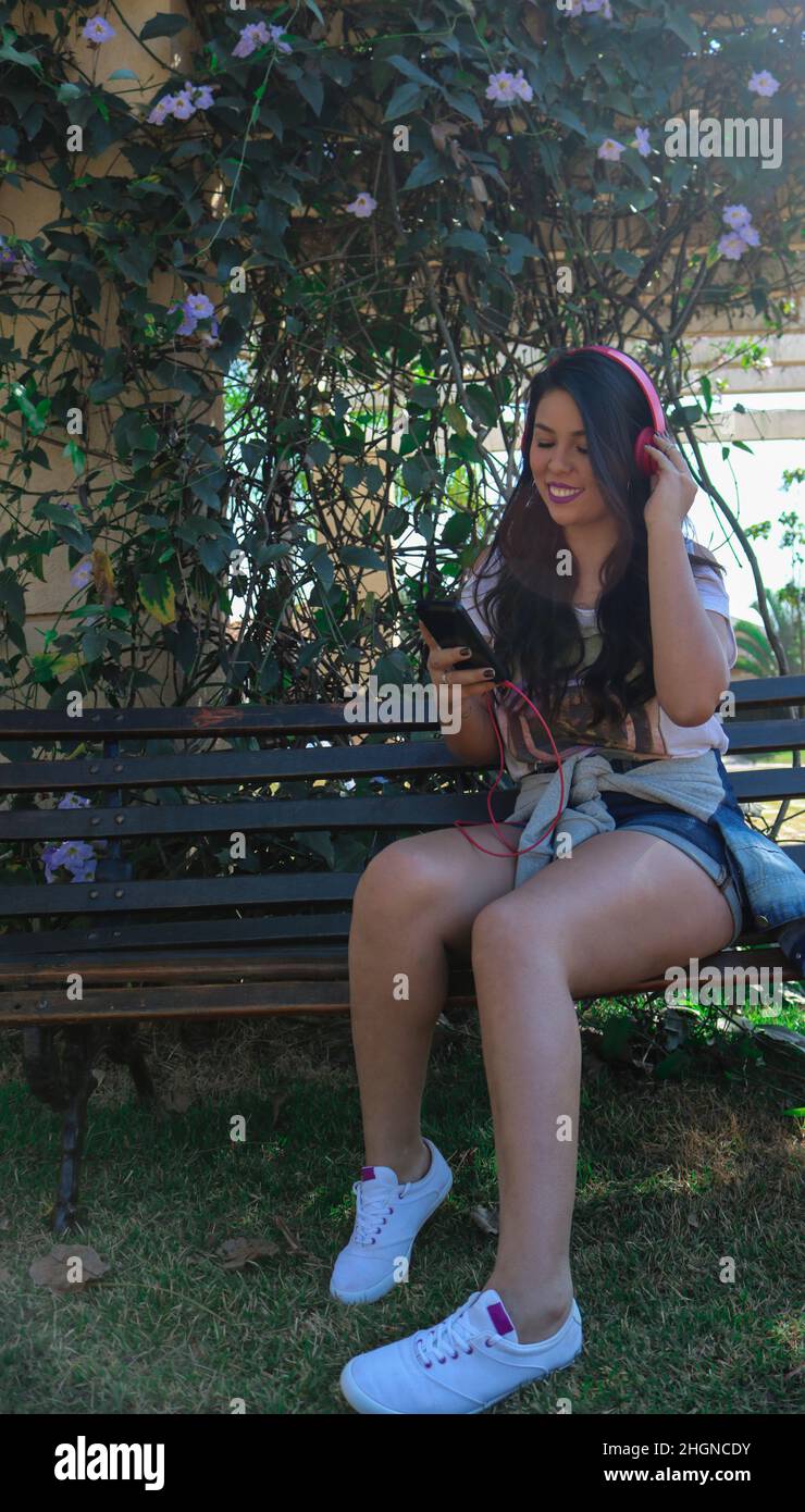 Belle jeune fille adolescente portant un casque et utilisant une tablette dans un parc. Banque D'Images
