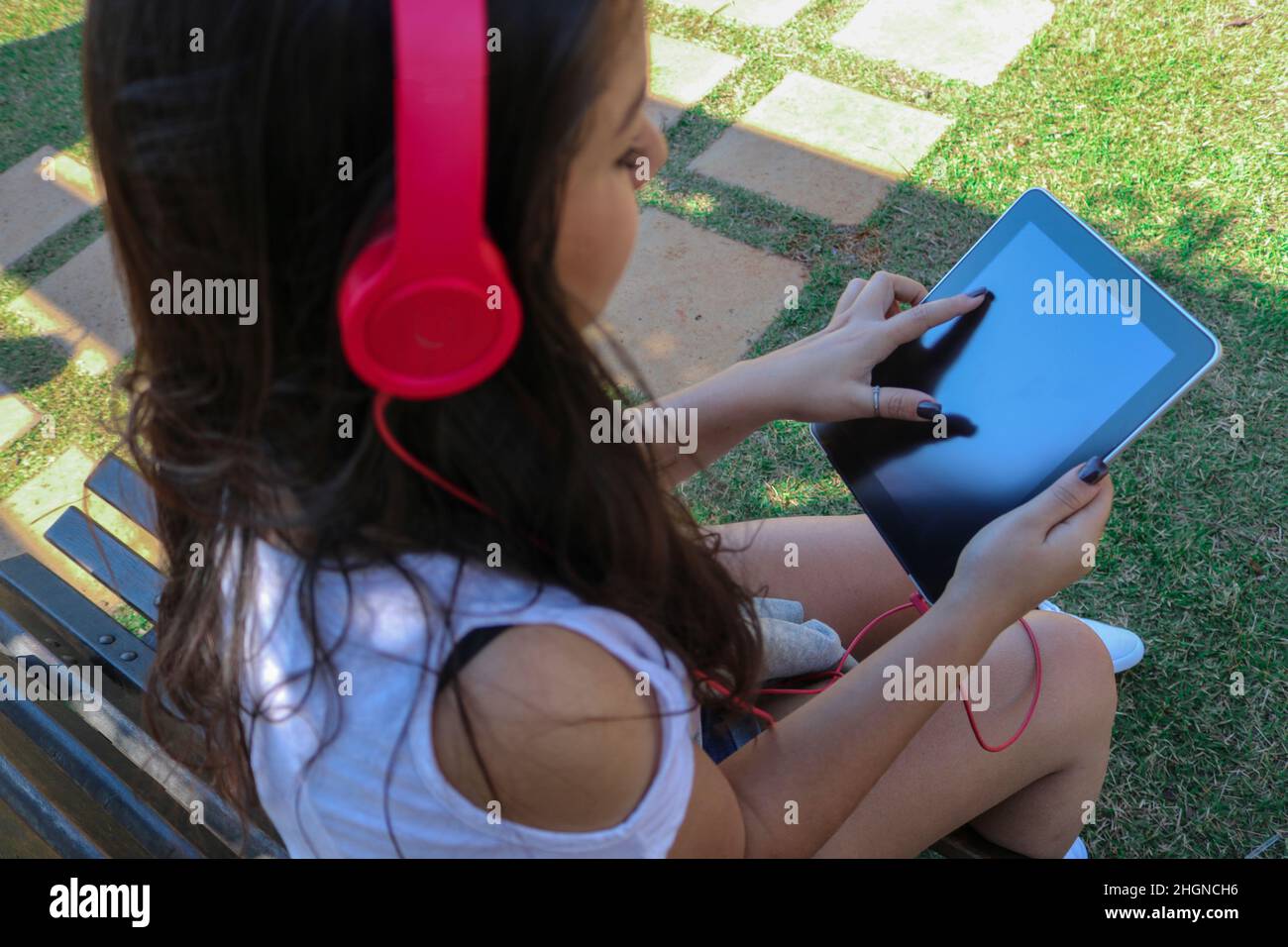 Belle jeune fille adolescente portant un casque et utilisant une tablette dans un parc. Banque D'Images