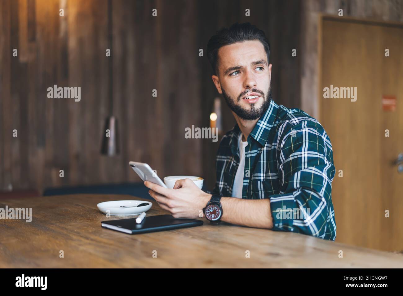 Un blogueur mâle de Caucaisan utilisant l'application de smartphone pendant le temps de café à l'intérieur du café Banque D'Images