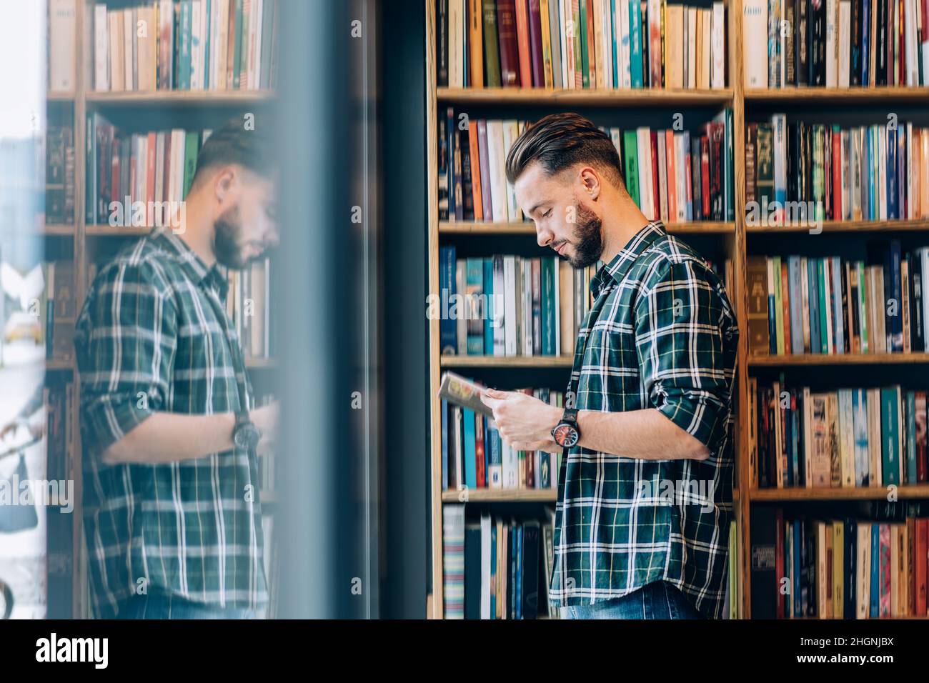 Vue latérale d'un étudiant de race blanche dans des vêtements décontractés lisant le meilleur roman vendeur dans la librairie publique Banque D'Images