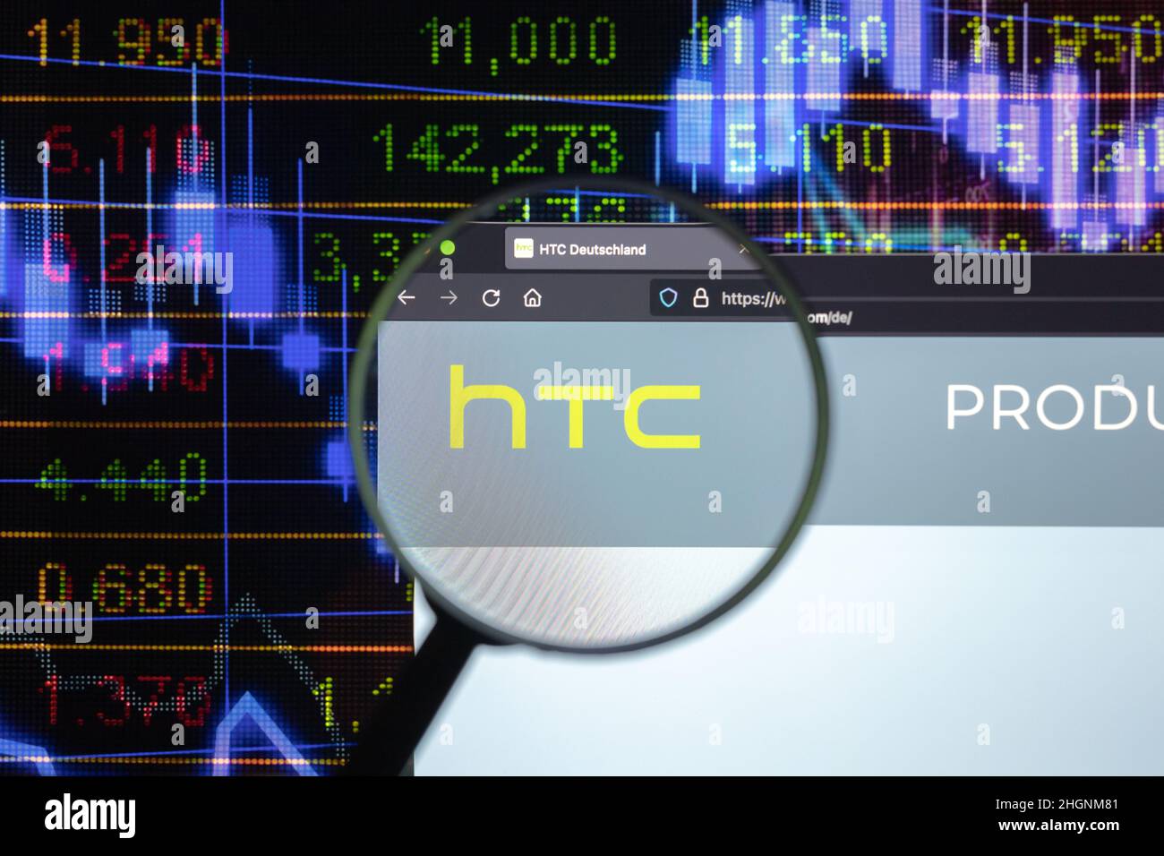 Logo de la société HTC sur un site web avec des développements flous de marché boursier en arrière-plan, vu sur un écran d'ordinateur à travers une loupe. Banque D'Images