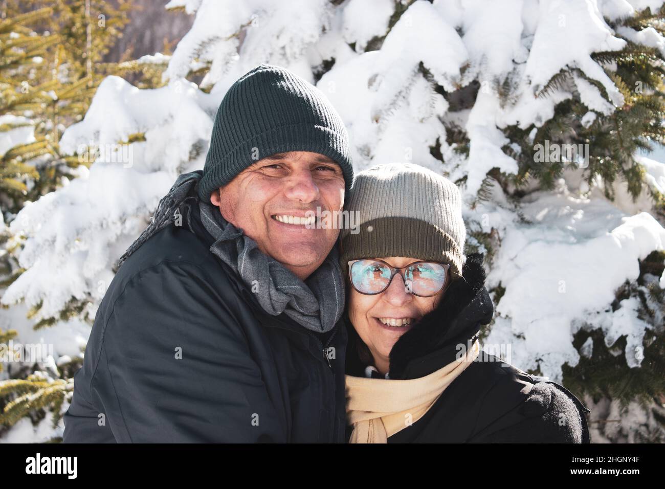 Couple d'âge moyen en vêtements d'hiver se serrant les uns les autres et montrant de l'affection.Couple caucasien souriant ensemble entre la neige et la forêt.Candi Banque D'Images