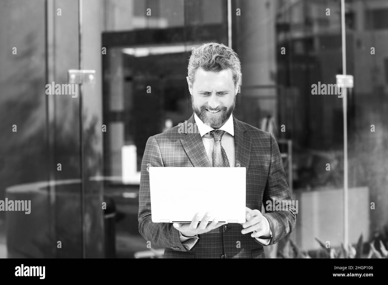 Homme d'affaires tenant un ordinateur portable debout dans la rue près du bureau d'affaires. Banque D'Images