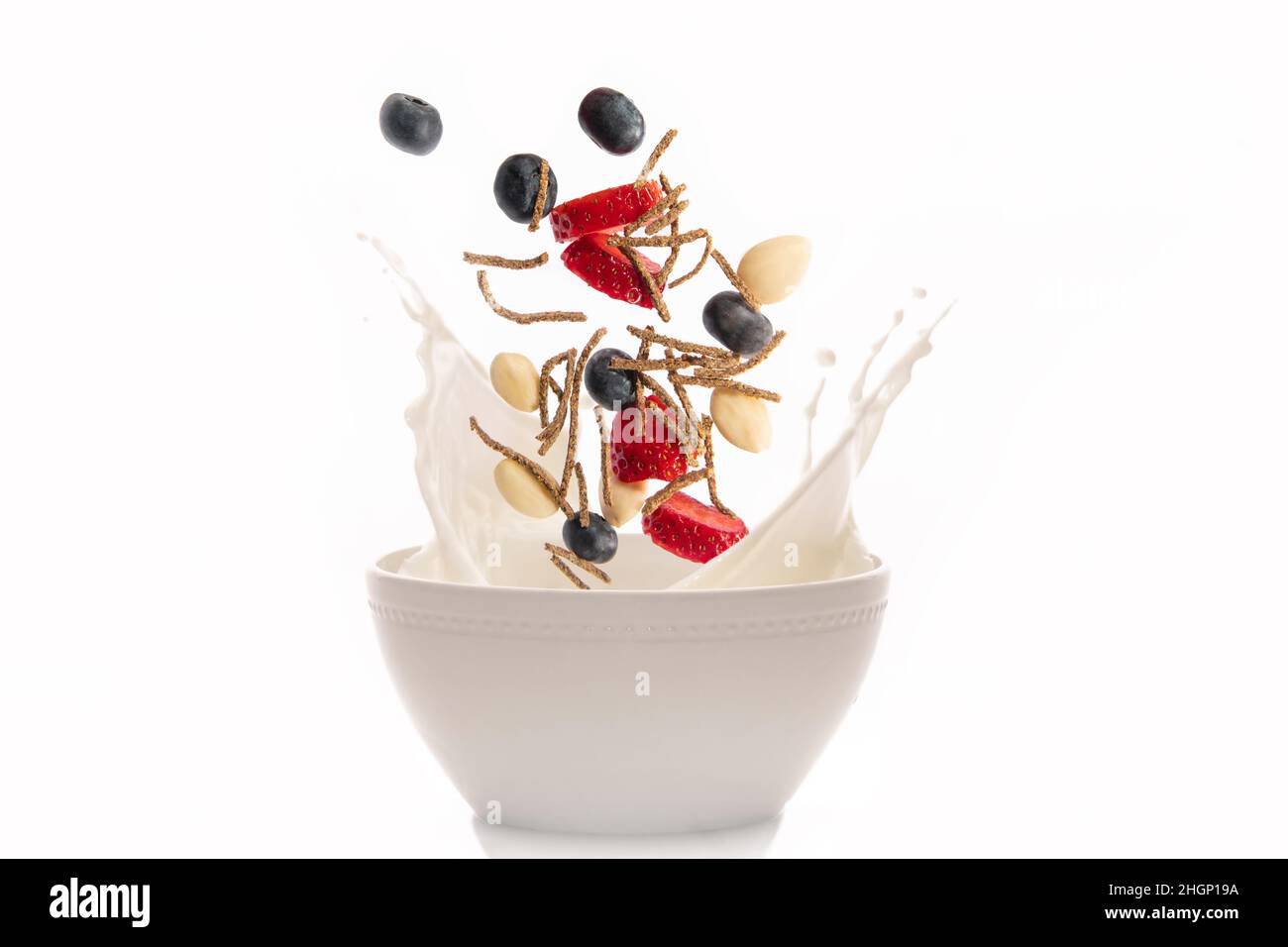 Fibres de céréales avec fraise, amandes et myrtille tombant et éclaboussant dans un bol avec du lait Banque D'Images
