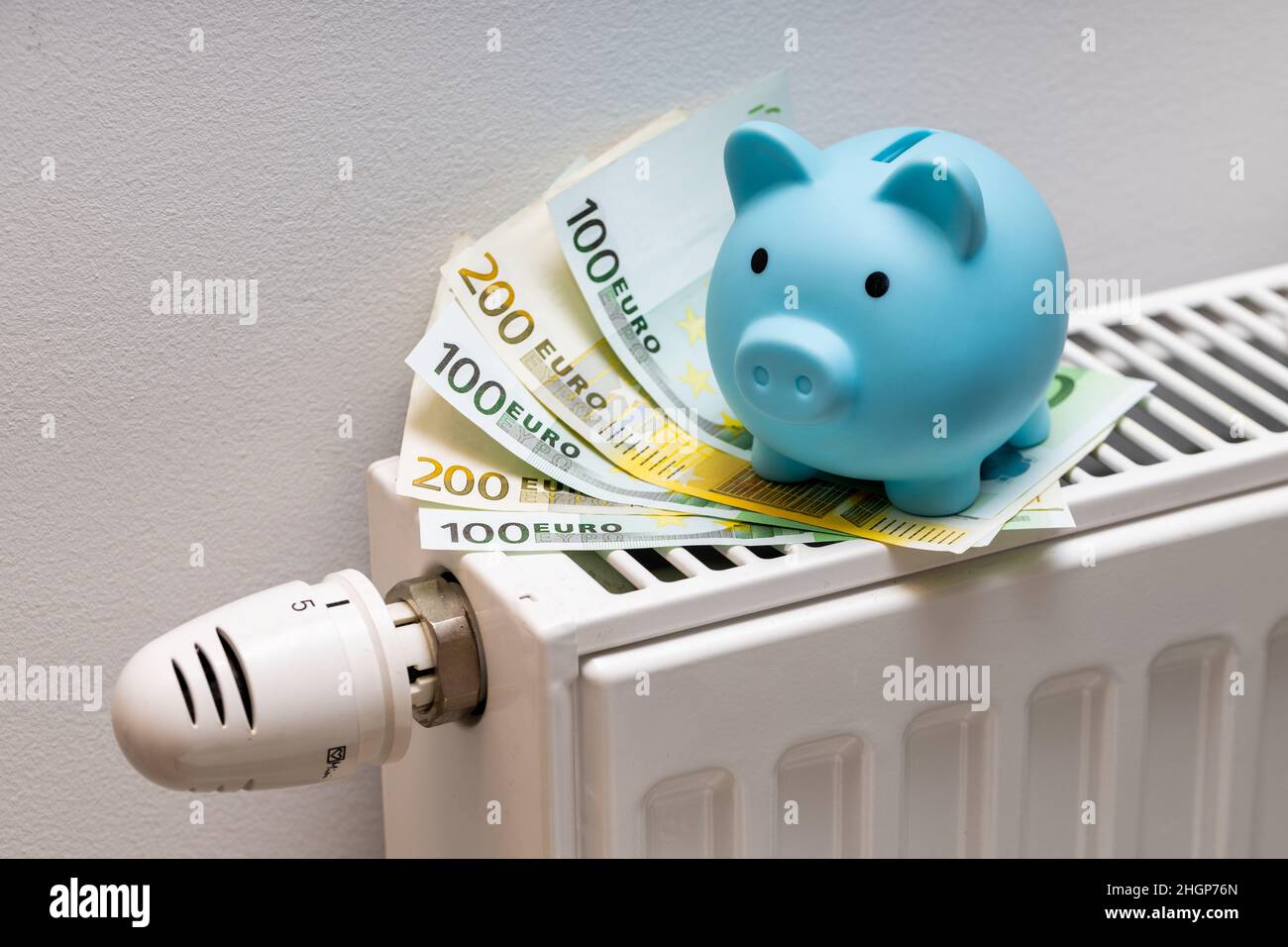Billets de 100 et 200 euros couchés sur le radiateur avec une petite banque de porc bleue, le concept de la hausse des coûts de chauffage d'un appartement en Europe Banque D'Images