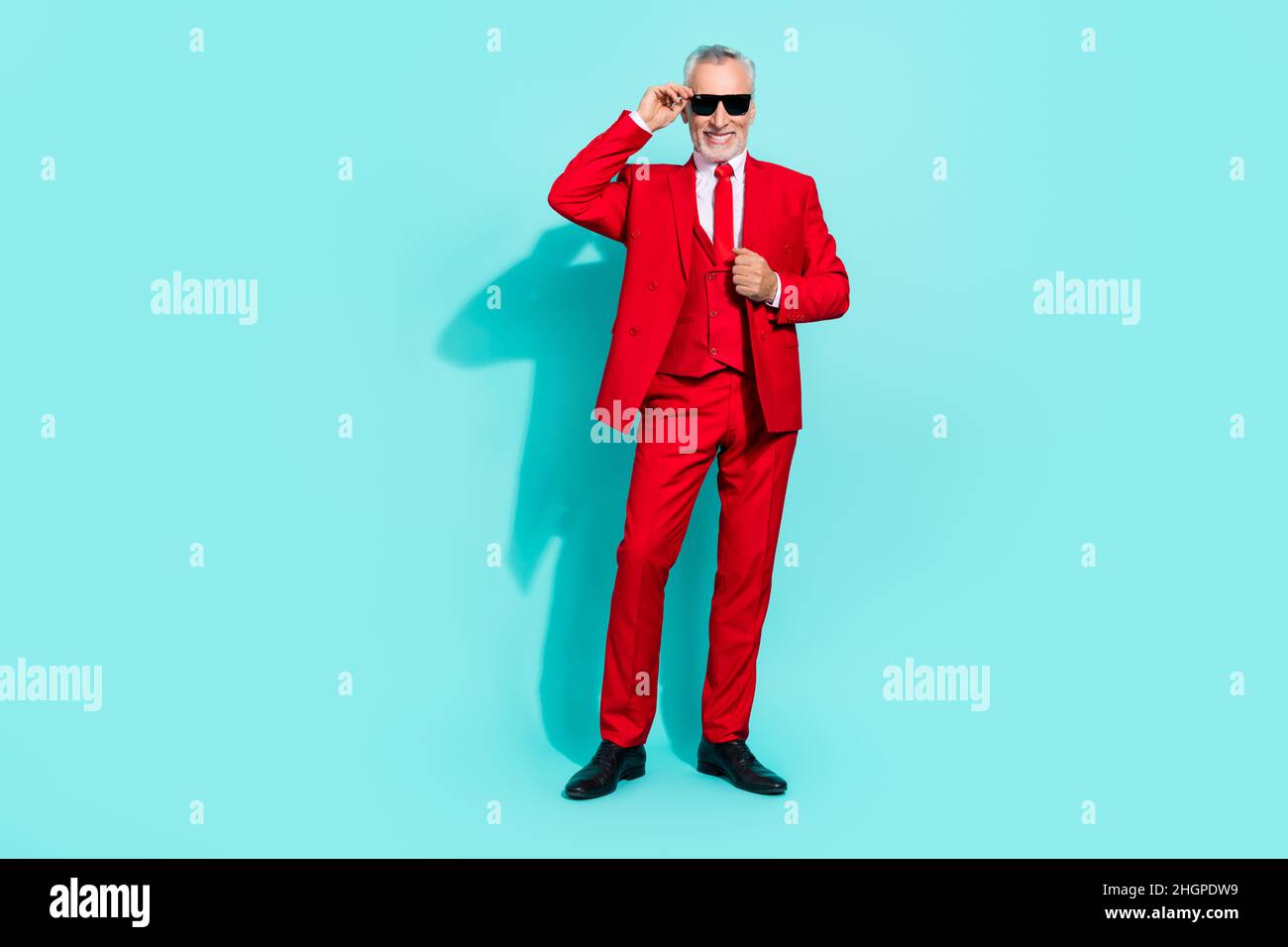 Photo de joli retraité homme porter un costume rouge trois pièces bras lunettes foncé souriant isolé couleur turquoise arrière-plan Banque D'Images