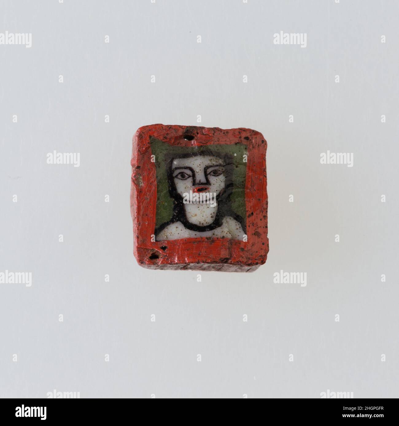 Inlay / perle blanc avec face 100 BC–100 AD période Ptoléméenne–période romaine Une technique de mosaïque de verre a permis de créer des multiples d'une image: Une composition figurale ou design a été faite en regroupant des cannes en verre coloré, qui ont ensuite été tirées dans une longue barre.La barre a ensuite été sectionnée à angle droit, probablement en frappant la barre avec les outils appropriés, pour produire de petits carreaux incrusts.Le carreau serait alors lissé et poli sur la face destinée à apparaître vers l'extérieur.Incrustation / cordon avec face.100 BC–100 AD.Verre.Période Ptolemaic–période romaine.De l'Égypte Banque D'Images