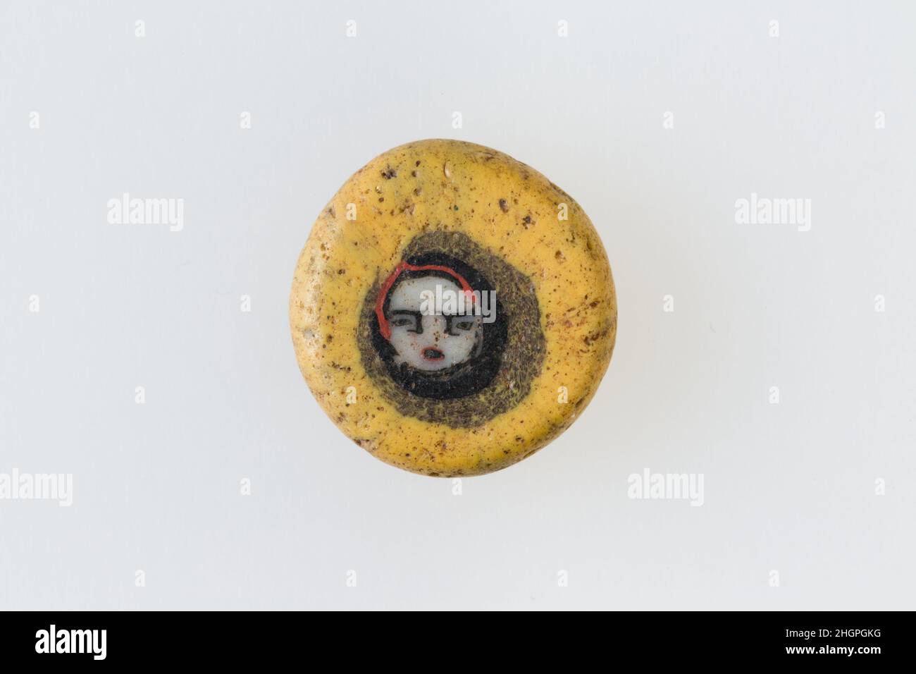 Inlay / perle blanc avec face 100 BC–100 AD période Ptoléméenne–période romaine Une technique de mosaïque de verre a permis de créer des multiples d'une image: Une composition figurale ou design a été faite en regroupant des cannes en verre coloré, qui ont ensuite été tirées dans une longue barre.La barre a ensuite été sectionnée à angle droit, probablement en frappant la barre avec les outils appropriés, pour produire de petits carreaux incrusts.Le carreau serait alors lissé et poli sur la face destinée à apparaître vers l'extérieur.Incrustation / cordon avec face.100 BC–100 AD.Verre.Période Ptolemaic–période romaine.De l'Égypte Banque D'Images