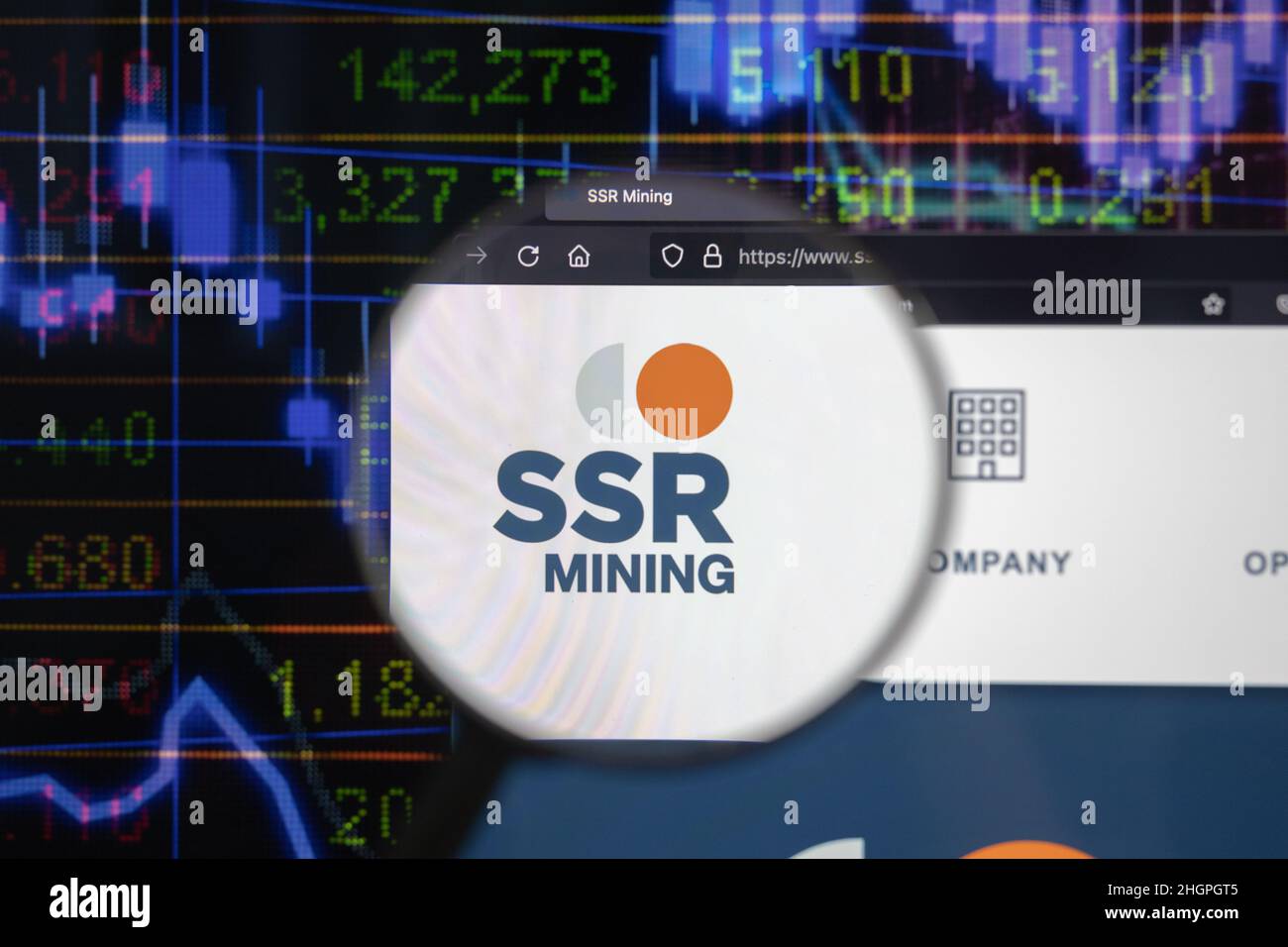 Logo de la société SSR Mining sur un site web avec des développements flous du marché boursier en arrière-plan, vu sur un écran d'ordinateur à travers une loupe. Banque D'Images