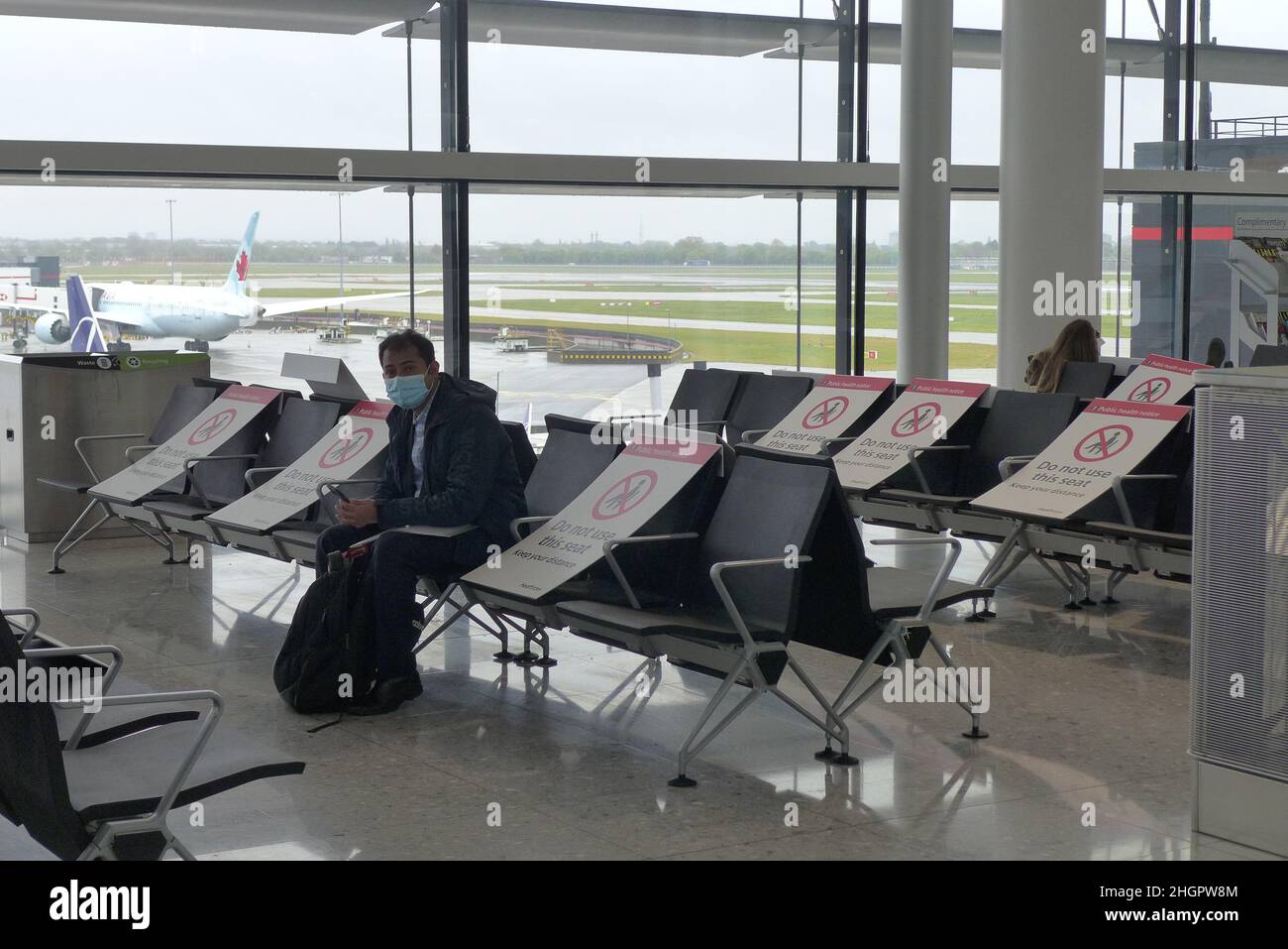 Aéroport international de Heathrow, Londres, Royaume-Uni - Mai 8 2021 : peu de passagers attendent à la porte avec en premier plan les chaises d'attente avec le panneau de signalisation Banque D'Images