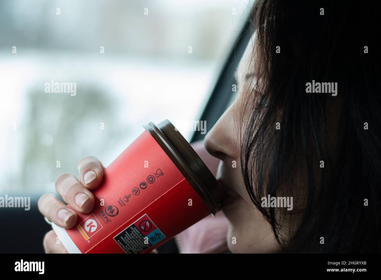 Femme aux cheveux noirs assise dans la voiture et buvant du café dans une tasse en papier recyclable Banque D'Images