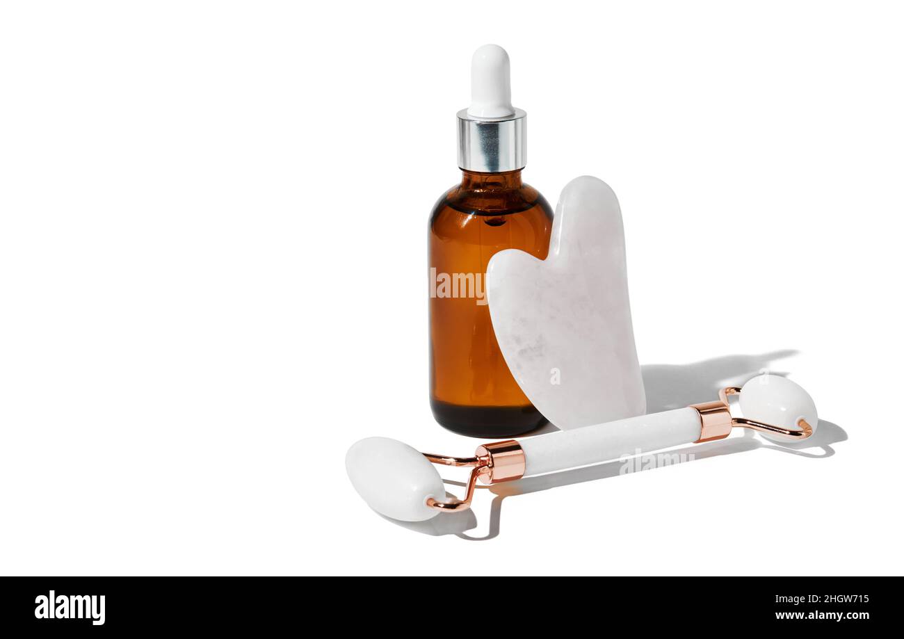 Outils de massage Gua Sha pour une meilleure circulation sanguine et l'huile essentielle isolée sur fond blanc avec passe-cheveux.Concept de soins de la peau à domicile. Banque D'Images