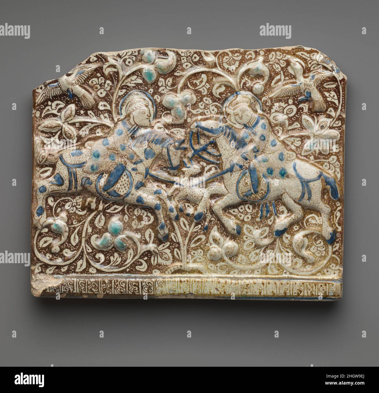 Carreau de frise avec deux chasseurs deuxième moitié 13th siècle ce carreau de frise est moulé en relief et peint en lustre sur un sol blanc opaque avec des accents de bleu turquoise et cobalt.L'arrière-plan présente un paysage luxuriant de motifs végétaux et d'oiseaux en vol, tandis qu'au premier plan deux cavaliers stab un cerf avec leurs épées.Les personnages portent des vêtements luxueux, et l'artiste a pris soin de représenter différents motifs textiles sur chacun.Des tuiles lustre de qualité, de couleurs et de motifs similaires décorent le palais à Takht-i Sulaymän, une importante résidence impériale Ilkhanid.Frise Ti Banque D'Images
