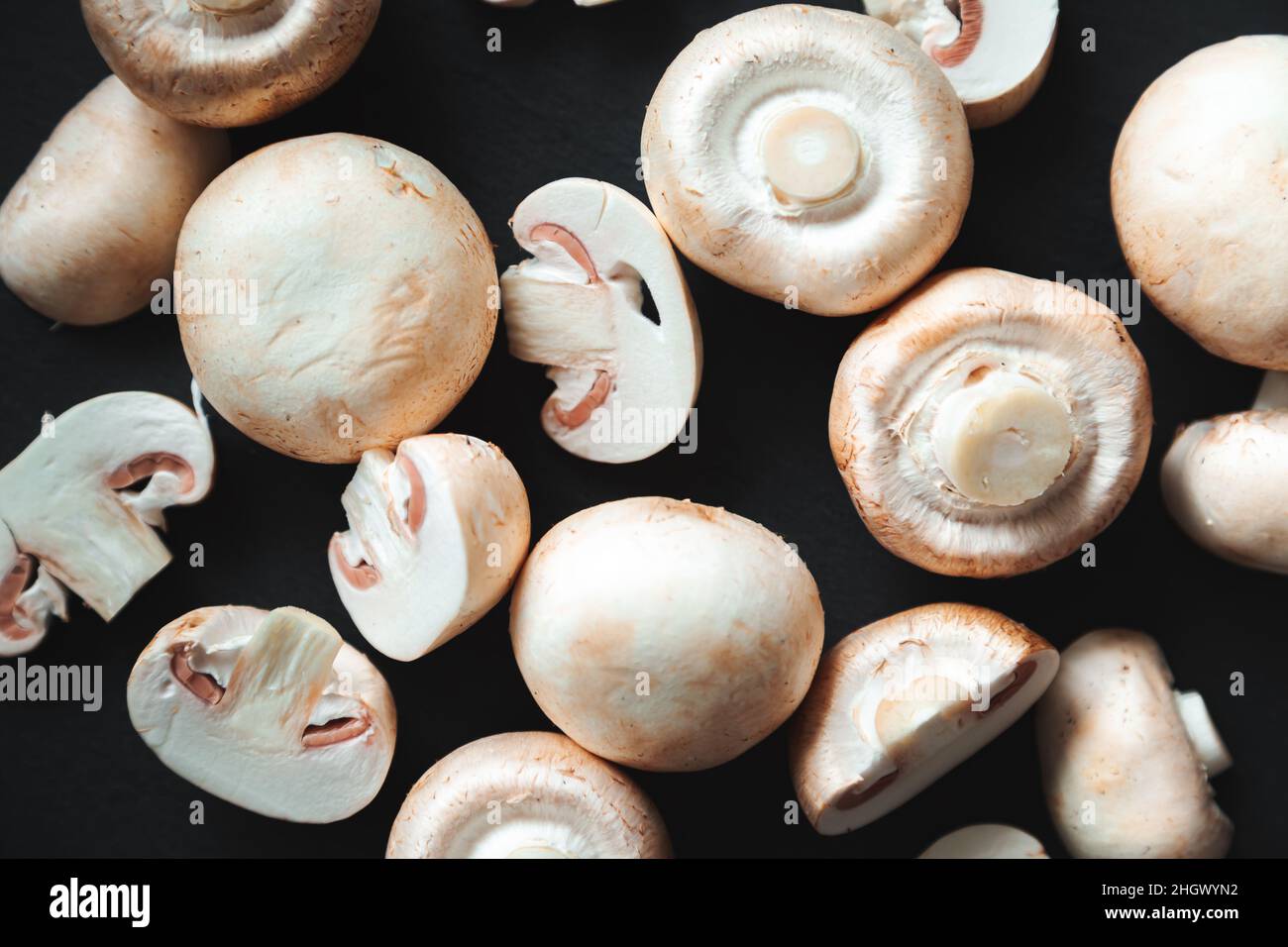 Champignons entiers et coupés sur fond noir.Gros plan, plat, vue de dessus.Contexte alimentaire, concentration sélective. Banque D'Images