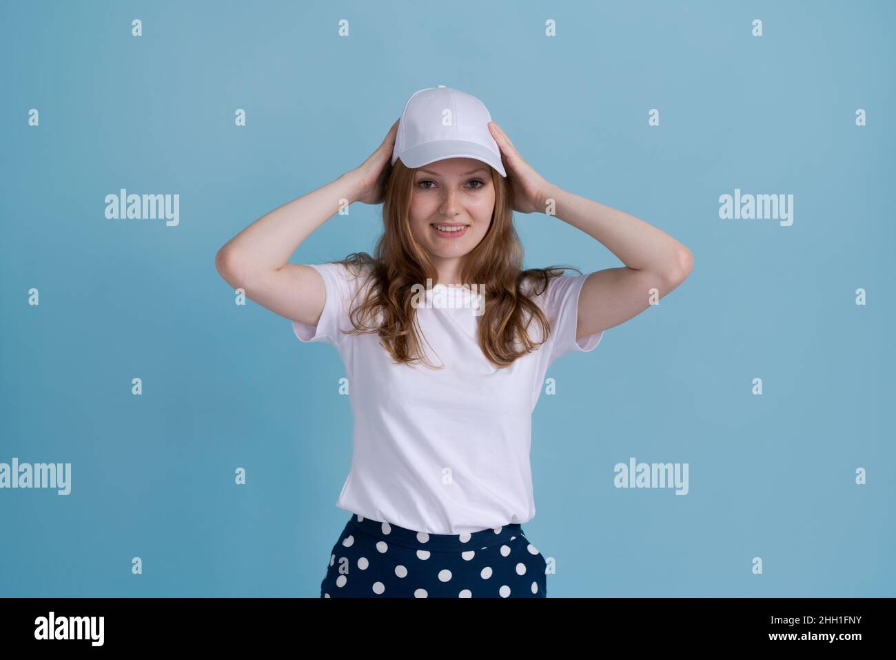 Jeune fille caucasienne en uniforme de livraison et casquette blanche  semble confiant avec le sourire sur son visage, pointant ses doigts  fièrement et heureusement, sur un fond bleu.Emplois pour les jeunes dans