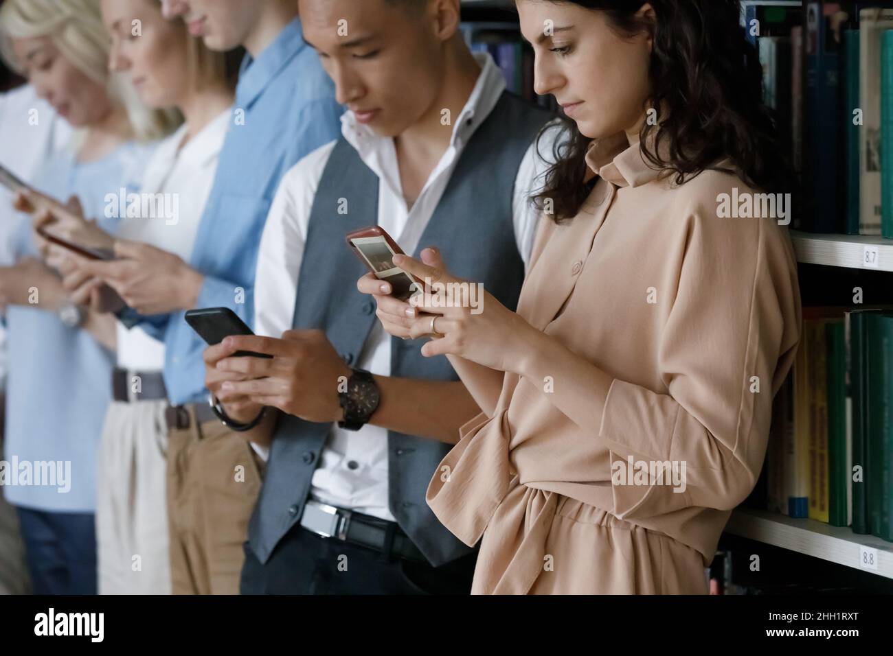 Groupe diversifié d'étudiants numériques dépendants debout sur des étagères Banque D'Images