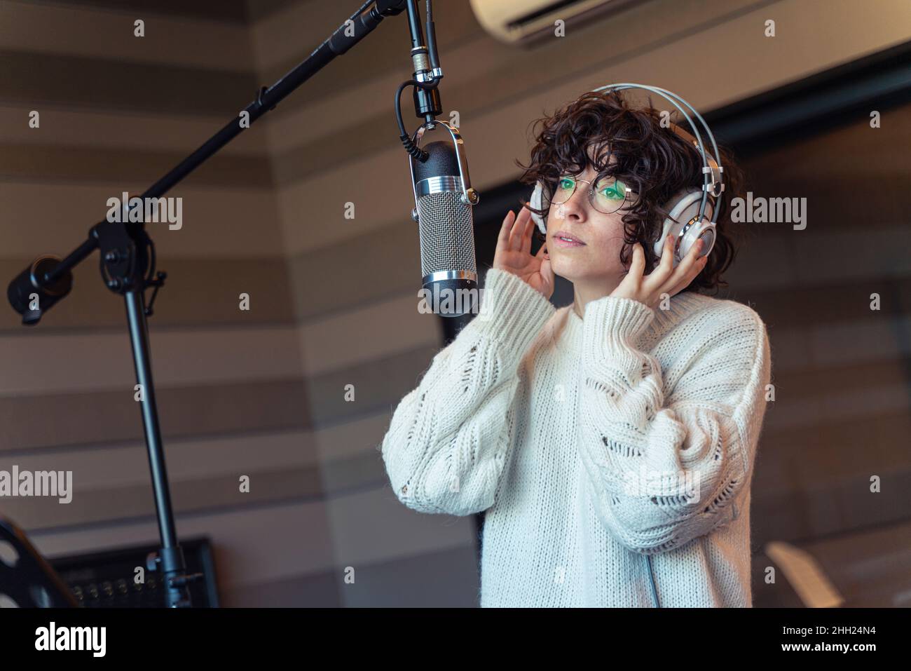 Une jeune chanteuse de cheveux bouclés avec des lunettes enregistrant une chanson dans un vrai studio Banque D'Images