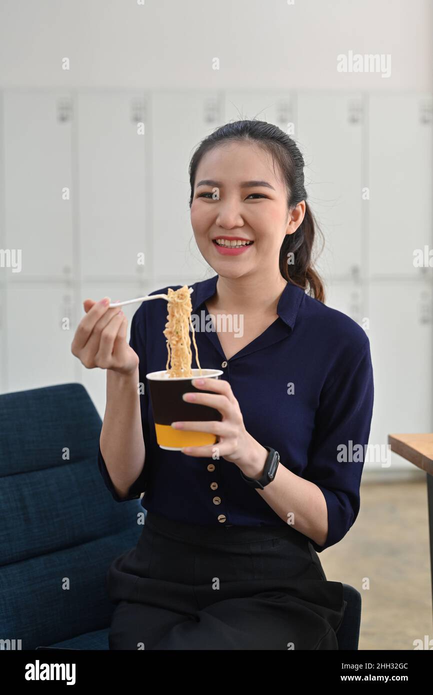 Femme asiatique souriante tenant une fourchette en plastique mangeant des nouilles instantanées au bureau. Banque D'Images
