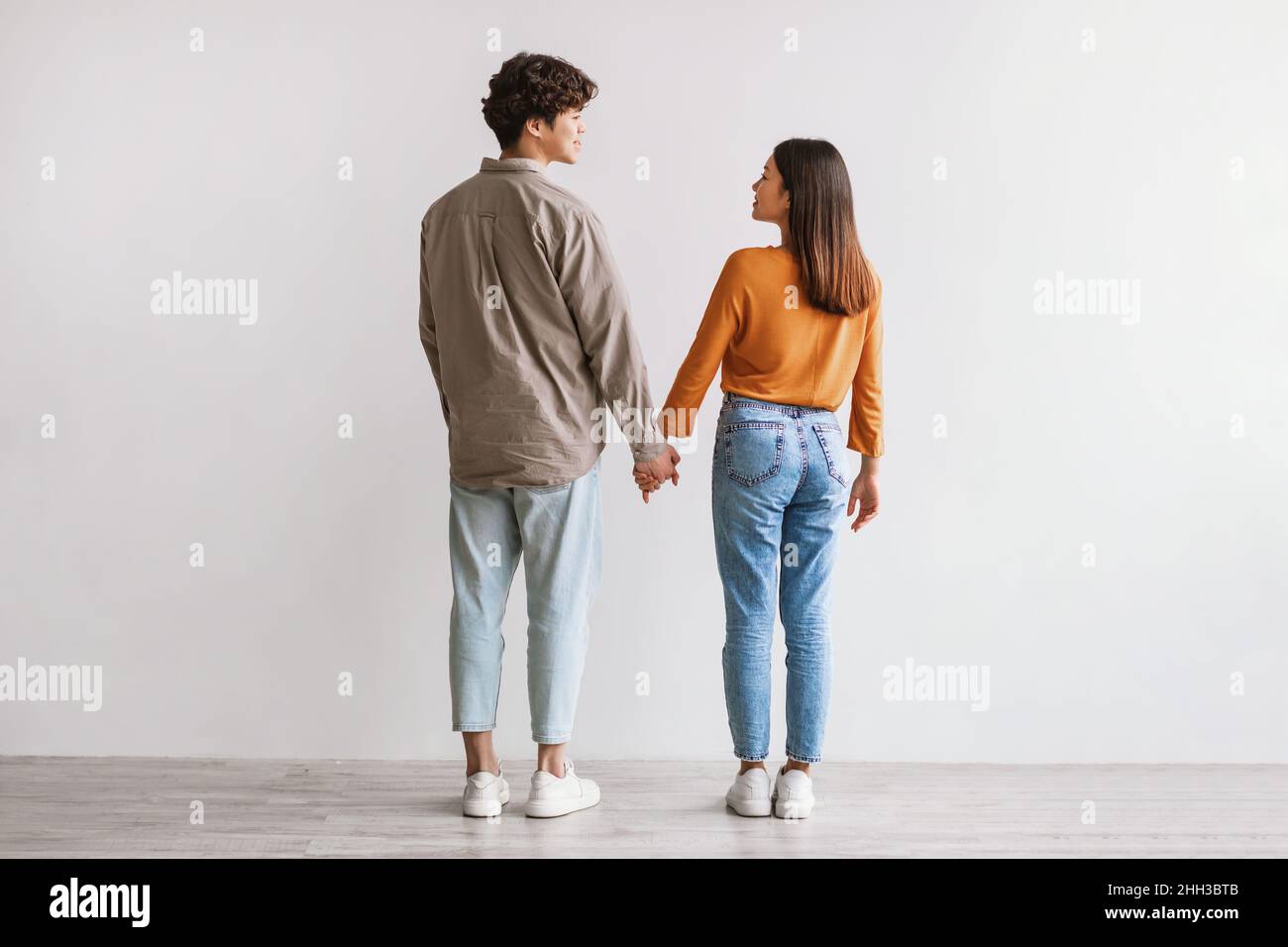 Pleine longueur de jeune asiatique homme et femme debout avec leur dos à la caméra, regardant les uns les autres et tenant les mains Banque D'Images