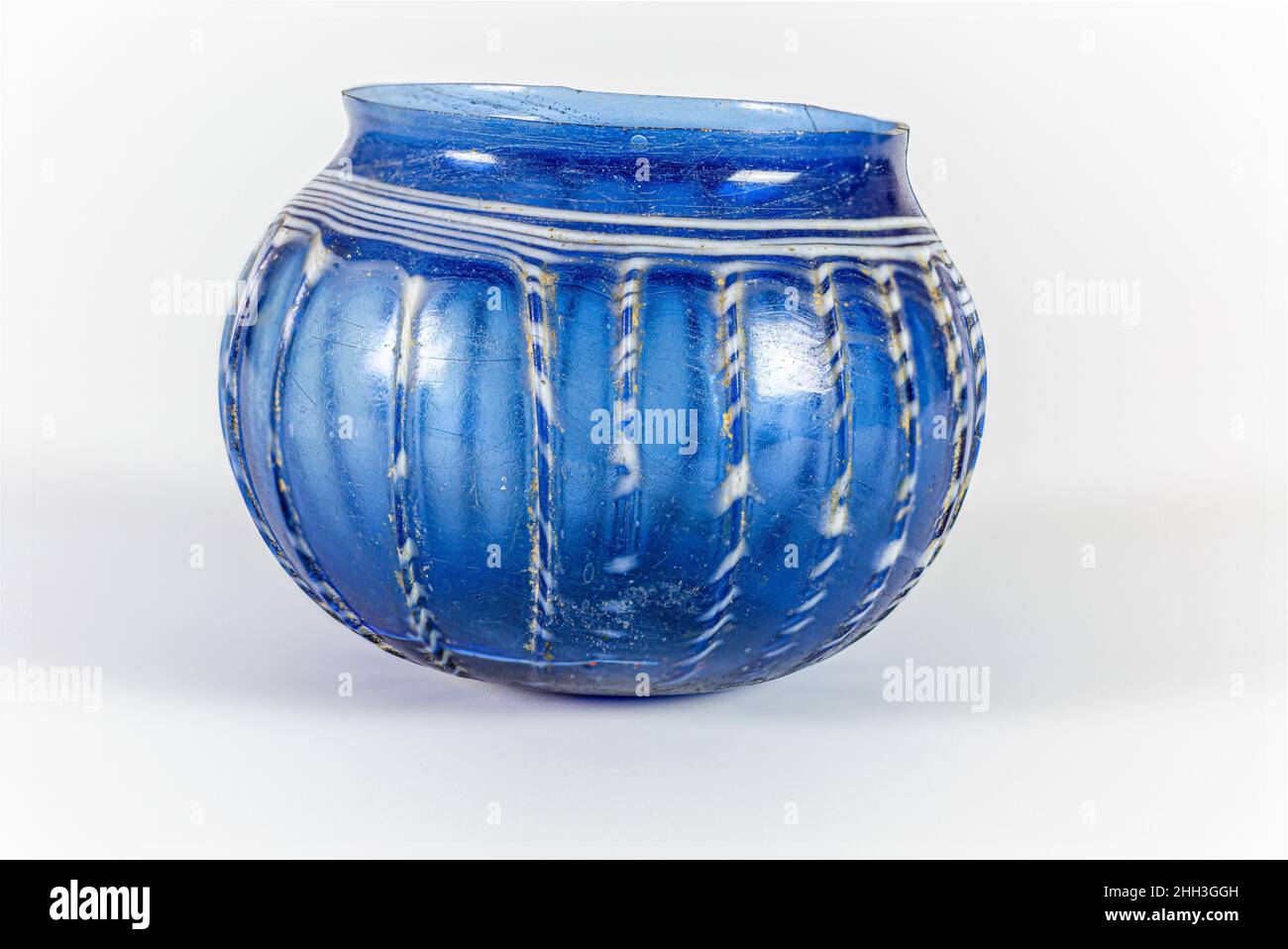 Bol côtelé en verre mi-1st Century A.D. Roman bleu cobalt translucide ; traînée en blanc opaque. Rebord rodé et inégal. Col concave court. Corps globulaire profond courbé à fond plat. Plaie striée spiralée autour du corps, avec grande surface circulaire sur le fond.Côtés en vingt-trois nervures verticales irrégulières. Brisés avec de grandes fissures autour du corps et une petite puce dans le rebord; quelques bulles; morcellement, piqûres, faible iridesence,et l'altération de la traînée autour du bas du corps et entre les nervures.Bol en verre côtelé.Romain. Mi-1st siècle A.D..Verre ; soufflé, traîné et outillaté.Début de l'Impériale.Verre Banque D'Images