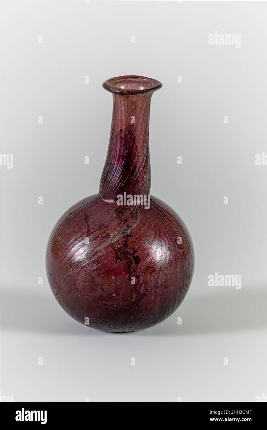 Flacon de parfum en verre 1st Century A.D. Roman translucide violet foncé; lignes blanches opaques.rebord éverté, replié et intérieur; col cylindrique, extensible vers le bas, avec un retrait horizontal à outils autour de la base; corps globulaire;Petit, fond plat.décor de sentier marré sur tout le corps du bord au fond, dont la plupart est maintenant absent jusqu'en devitrification.Complete, mais fissures dans le corps; bulles de piquer; piqûres profondes sur l'extérieur, épais brun des intempéries et brillant irience à l'intérieur.Flacon de parfum en verre.Romain.1st siècle A.D..Verre ; soufflé et traîné.Début de l'Impériale.Verre Banque D'Images