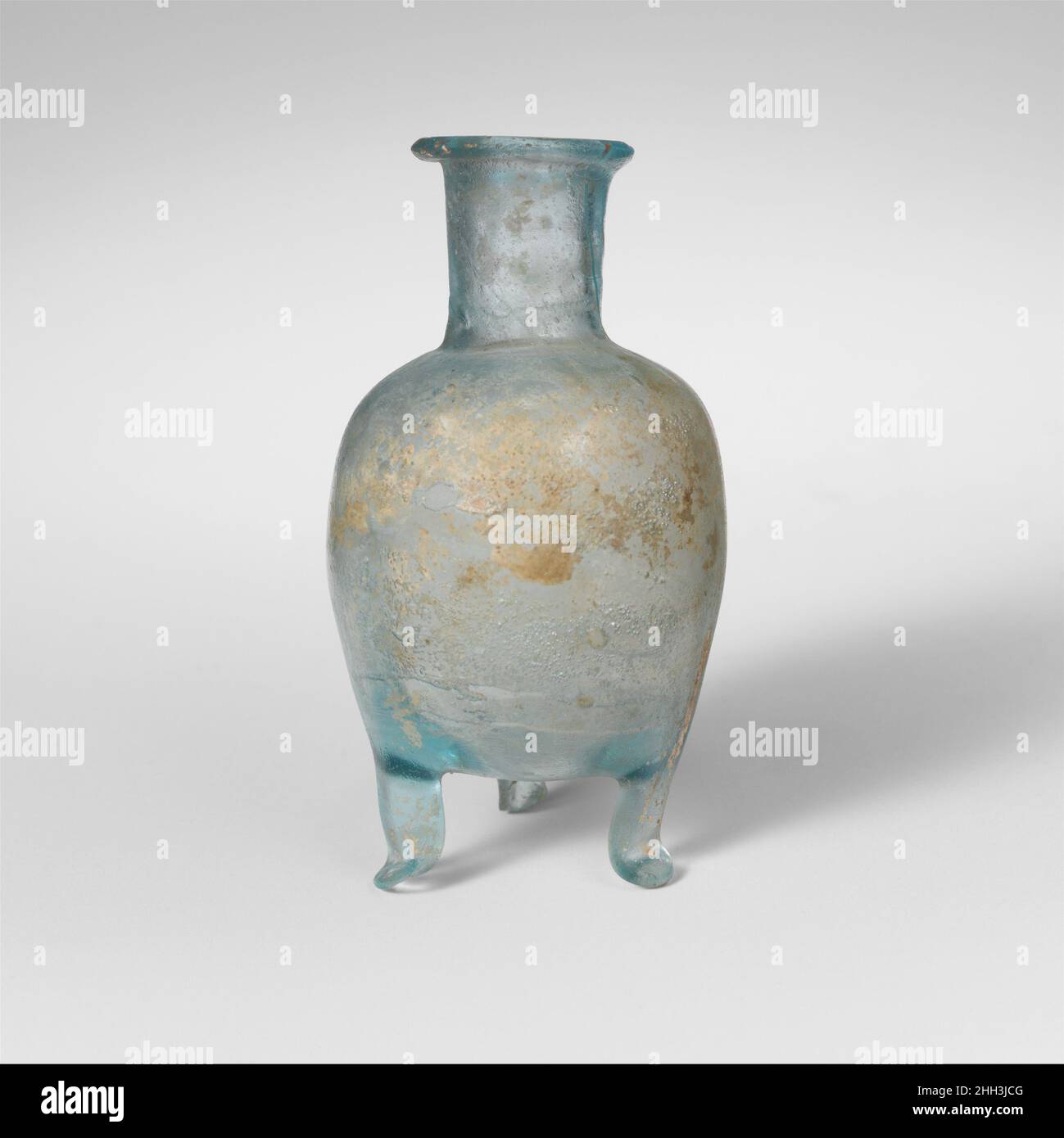 Flacon en verre avec trois pieds mi-1st Century A.D. Roman Translucent bleu pâle.rebord solide avec rebord horizontal à lèvres persistantes; col cylindrique, légèrement incliné vers le bas; épaule inclinée; corps ovoïde tronqué avec trois tiges solides autour de la base, étirées et outilées, se terminant par des pieds éclaboussés et pincés;Fond légèrement arrondi avec indent.Complete irrégulier, sauf pour la partie inférieure d'une tige et le pied, et deux fissures allant du bord vers le corps; beaucoup de bulles pinpick; ternir, quelques piqûres, et des taches d'intempéries irisées.vase en verre soufflé bleuâtre avec trois pieds et le col court.Bouteille en verre avec t Banque D'Images