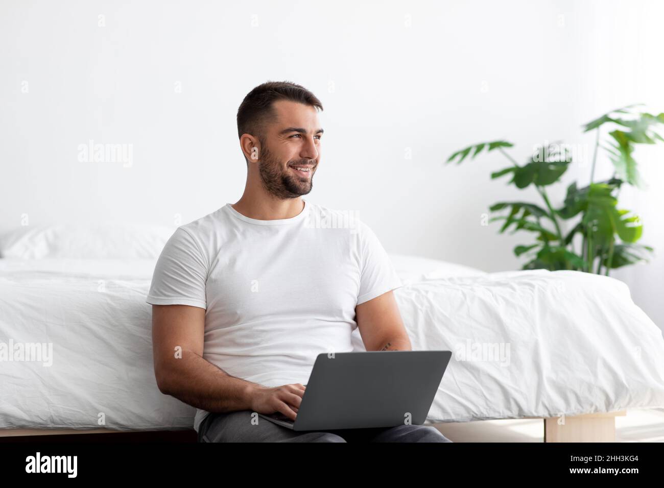 Joyeux jeune homme beau avec la barbe travail sur ordinateur portable et regarder l'espace vide Banque D'Images
