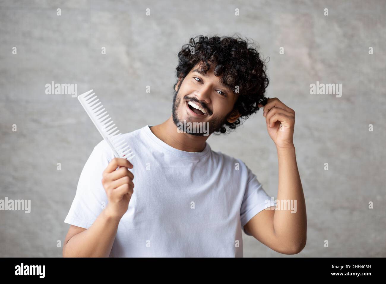 Soins à domicile après la douche, procédure matinale.Homme indien joyeux avec un peigne touchant des cheveux bouclés et sains Banque D'Images