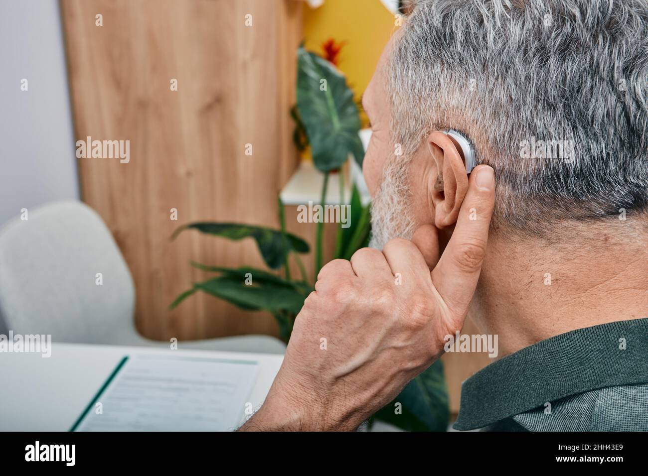 Solutions auditives pour les personnes âgées souffrant de surdité.L'homme plus âgé aux cheveux gris règle son aide auditive derrière l'oreille en appuyant sur le bouton de réglage avec son doigt Banque D'Images