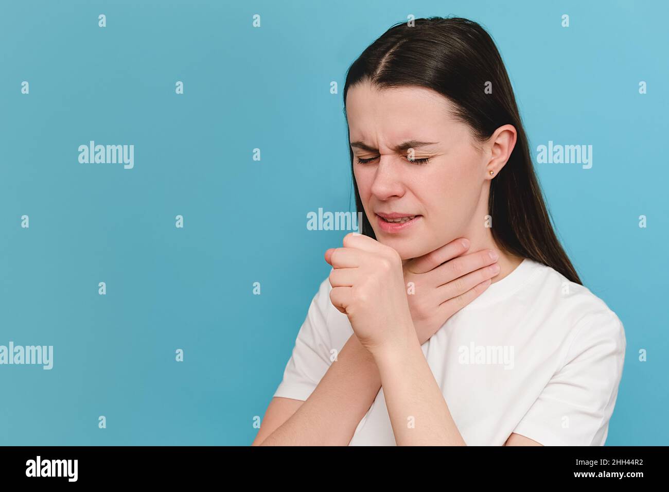 Une femme malsaine, isolée sur fond bleu, couvre sa bouche avec la main tout en toussant, souffre de grippe saisonnière ou de bronchite chronique Banque D'Images
