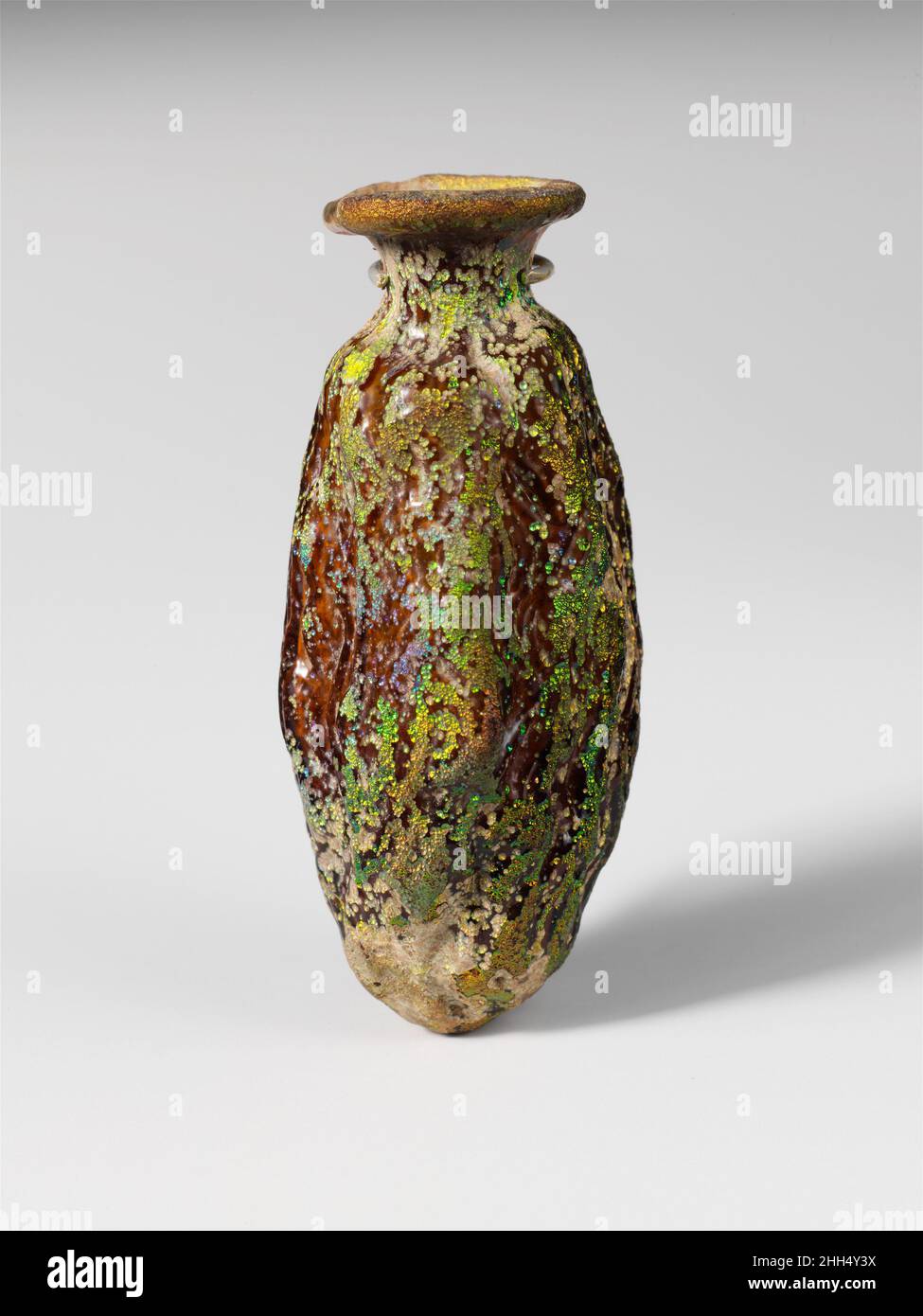 Flacon en verre en forme de date mi-1st–début de 2nd siècle A.D. Roman translucide brun jaunâtre.épais, rebord effilé plié rond et intérieur; bouche torrentie; col cylindrique court; corps allongé; fond pointu inégal.Un joint de moule continu autour du corps.corps moulé sous la forme d'une date ondulée, avec un motif de petites crêtes ondulées et creux.intact, à l'exception du petit trou abîmé dans le cou; morcellement, piqûres profondes, et iridesence brillante.Bouteille en verre en forme de date 245806 Banque D'Images