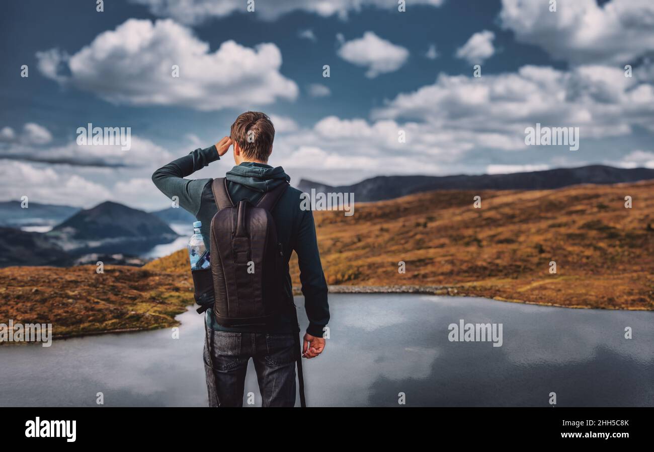 Jeune adulte homme randonnée regardant la vue avec le lac et la gamme de mountaing en arrière-plan, portant un sac à dos, vue arrière, debout, volda norvège Banque D'Images