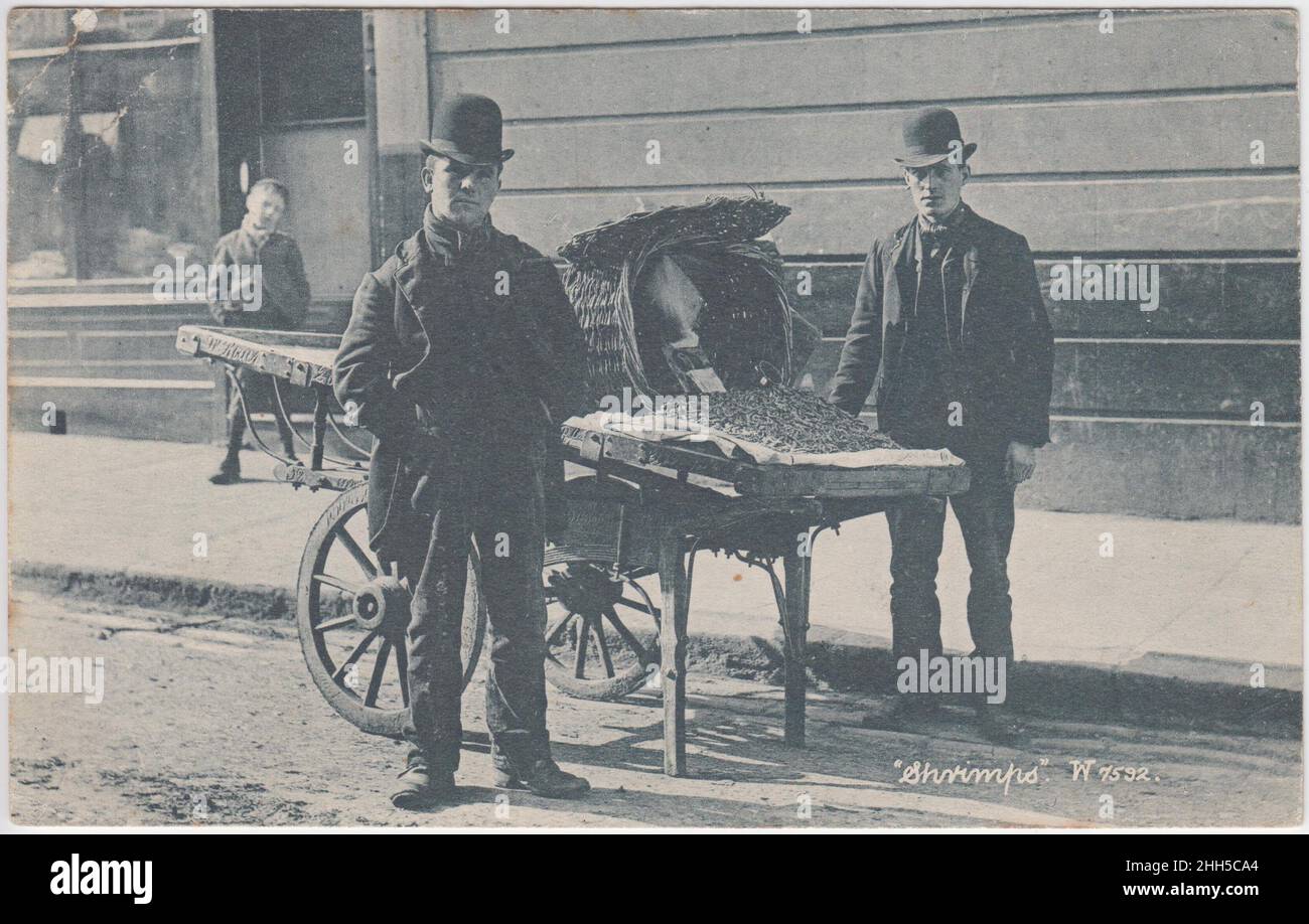 'Shrimps': Deux concombres qui vendent des fruits de mer à partir d'une charrette, un petit garçon frappe une pose en arrière-plan, au début du 20th siècle Banque D'Images