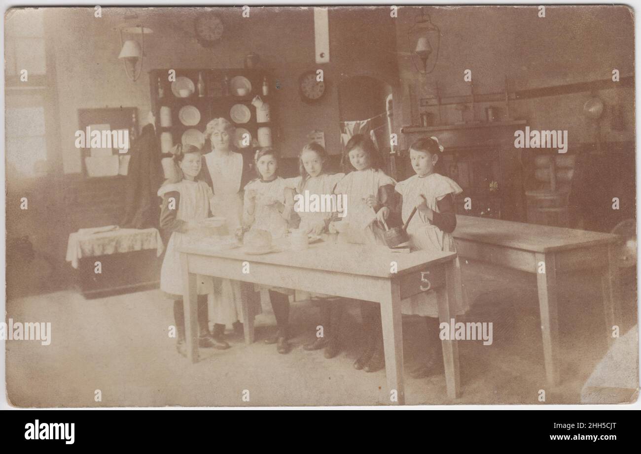 Les filles étant enseignées à cuisiner dans une cuisine scolaire, début du 20th siècle.L'équipement de blanchisserie peut être vu en arrière-plan, y compris une mangle Banque D'Images