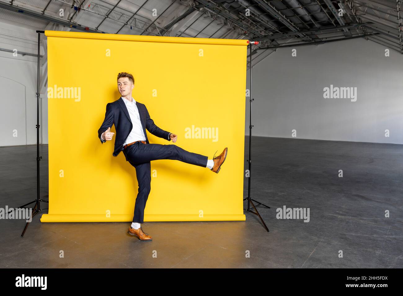 Homme d'affaires debout sur une jambe levant le pied devant un fond jaune Banque D'Images