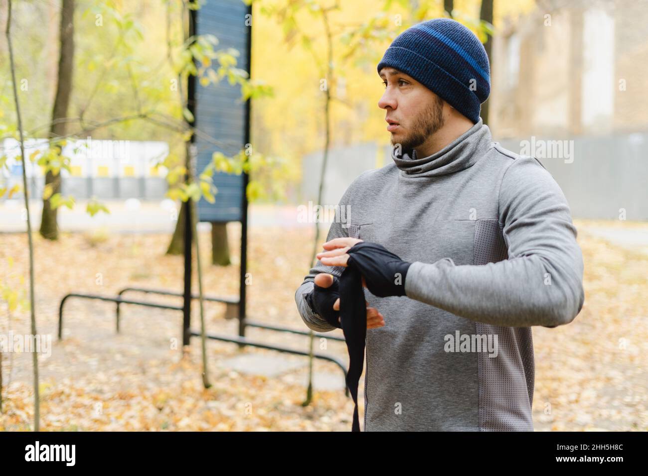 Jeune homme avec chapeau en tricot enveloppant bandage sur la main au parc Banque D'Images