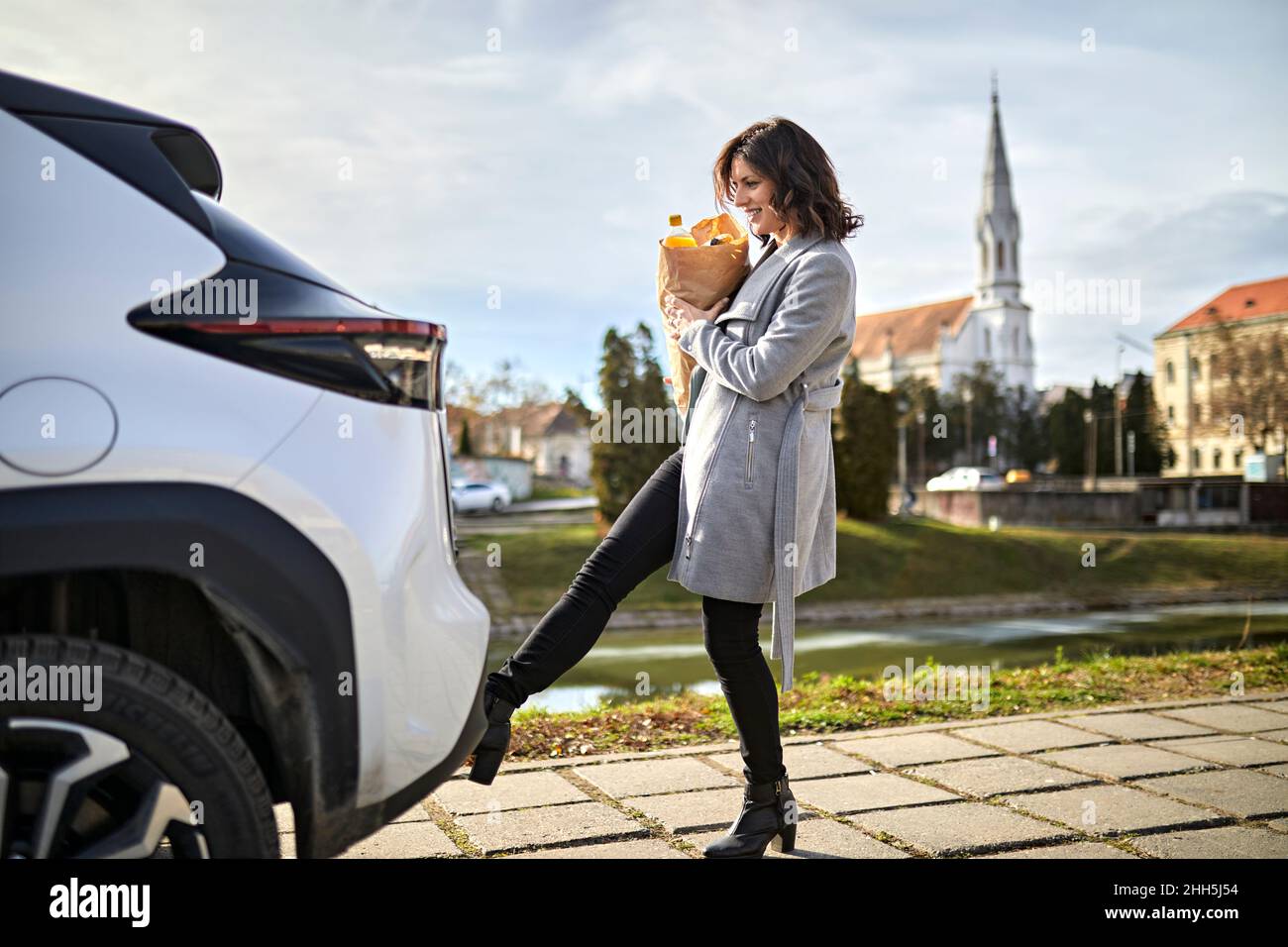 Femme porte un sac d'épicerie ouvrant le coffre de voiture avec capteur de pied Banque D'Images