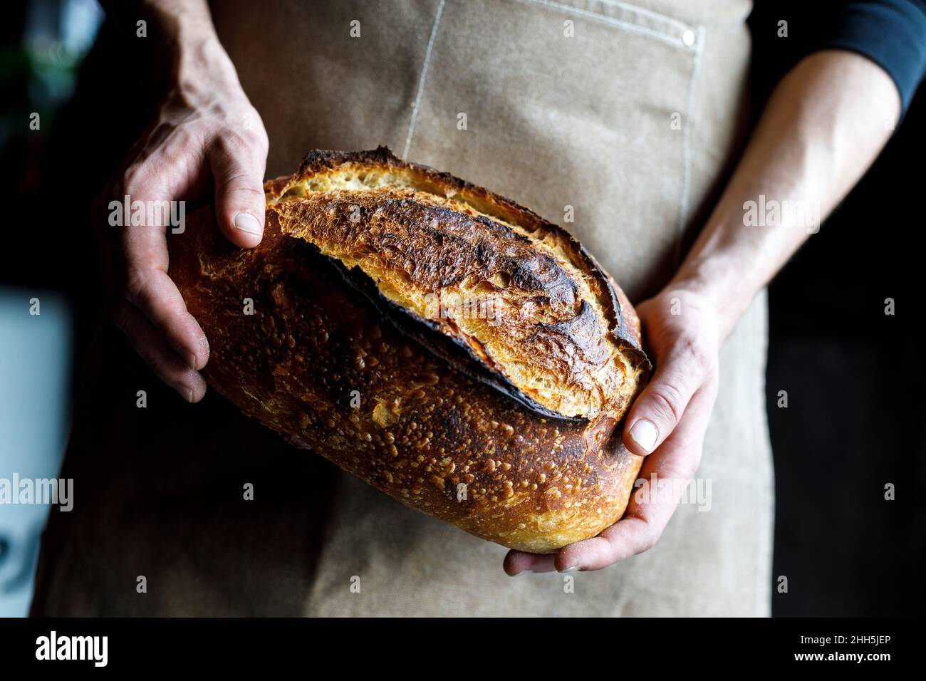 Baker portant un tablier contenant du pain de levain fraîchement cuit Banque D'Images