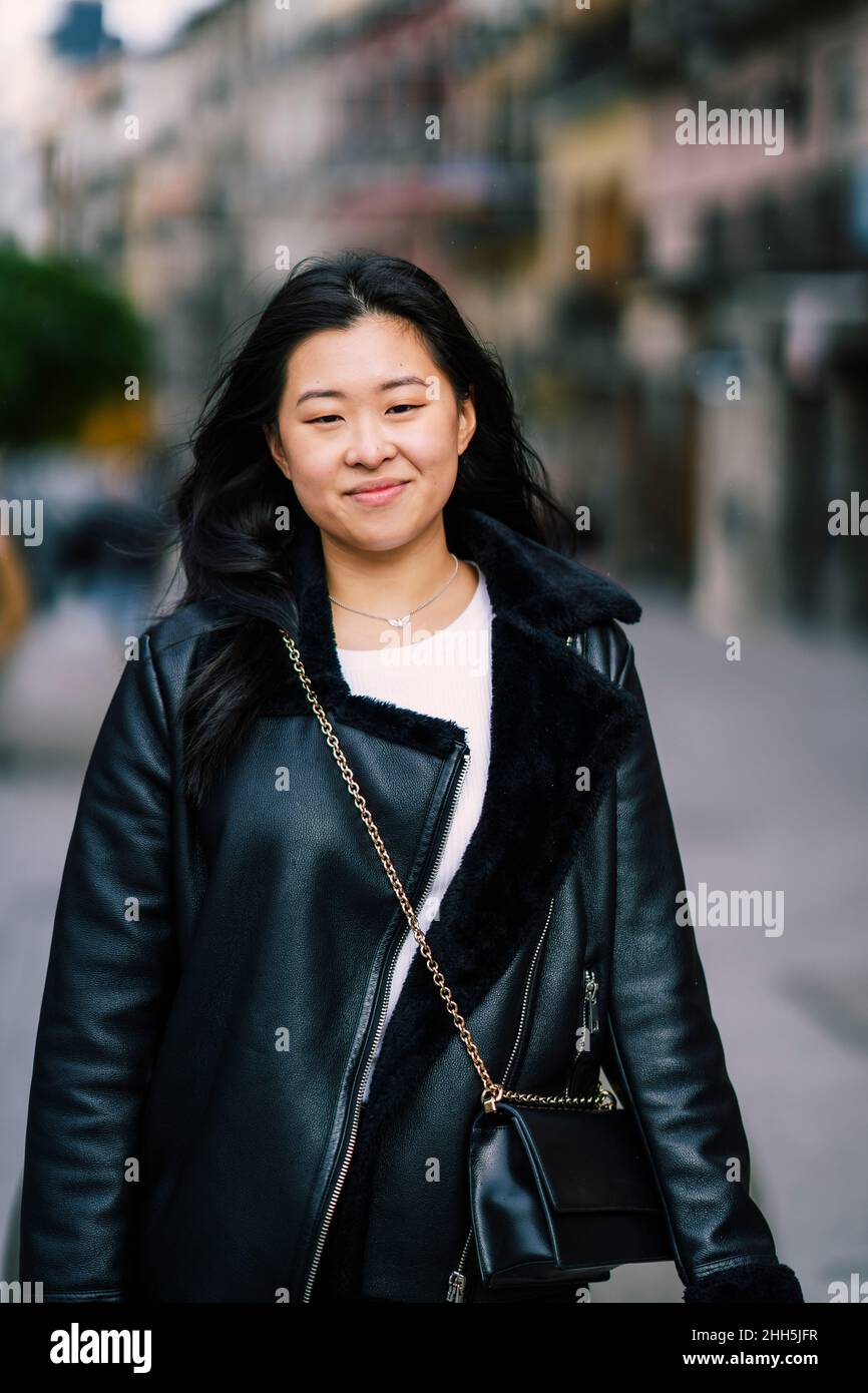 Jeune femme souriante portant un sac à bandoulière sur une veste noire Banque D'Images