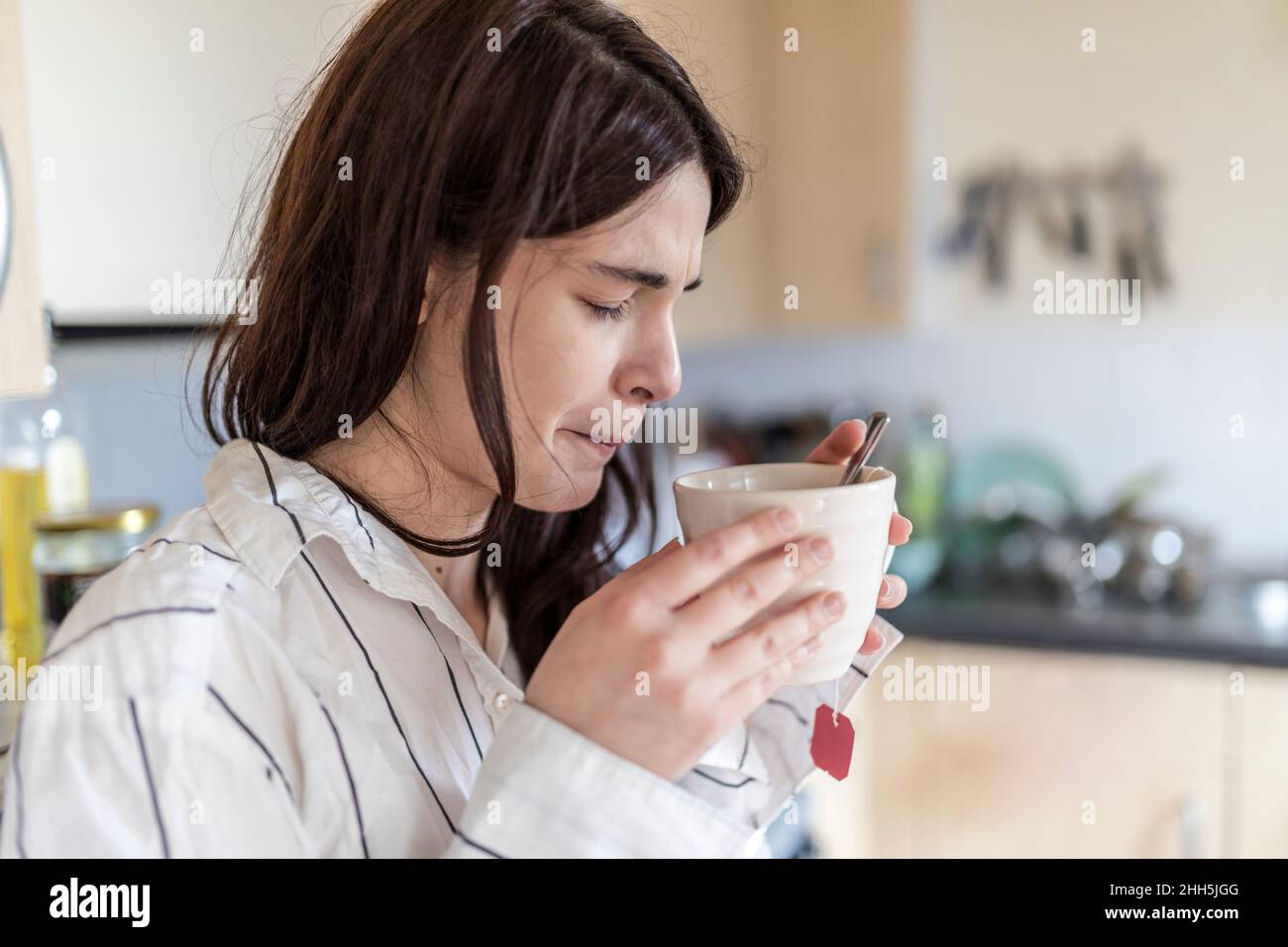 Femme avec les yeux fermés buvant du thé dans la cuisine à la maison Banque D'Images