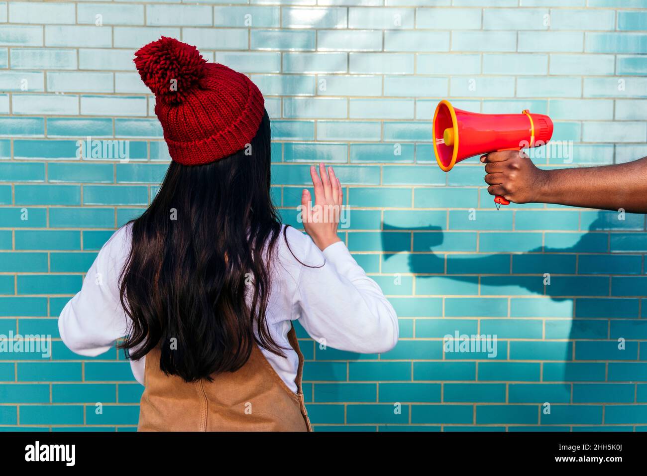 Main de l'homme tenant le mégaphone par une femme qui fait un geste devant un mur de briques turquoise Banque D'Images