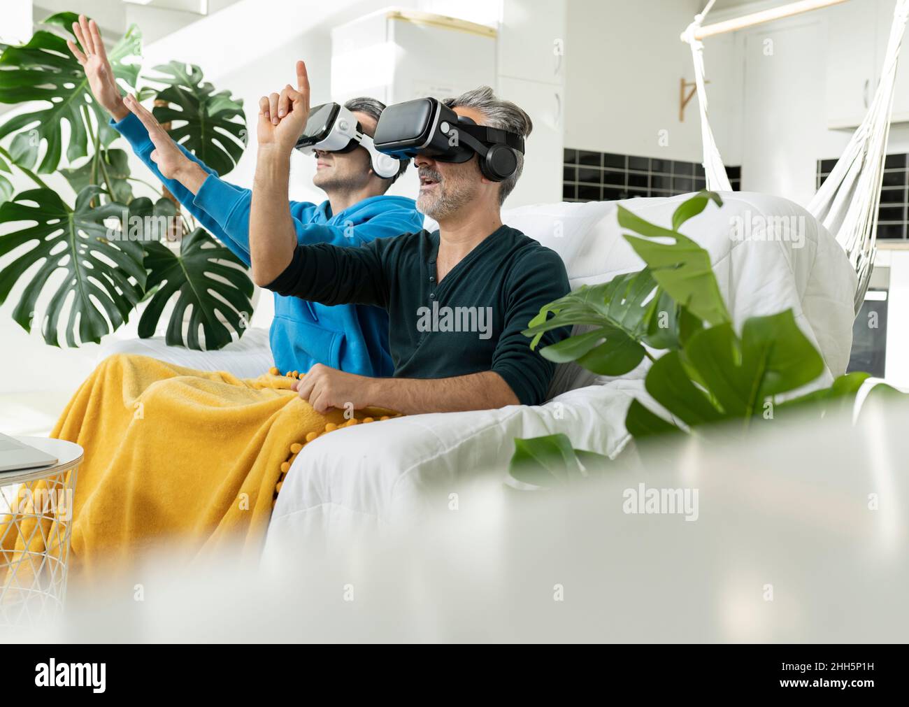 Couple gay utilisant des casques de réalité virtuelle à la maison Banque D'Images