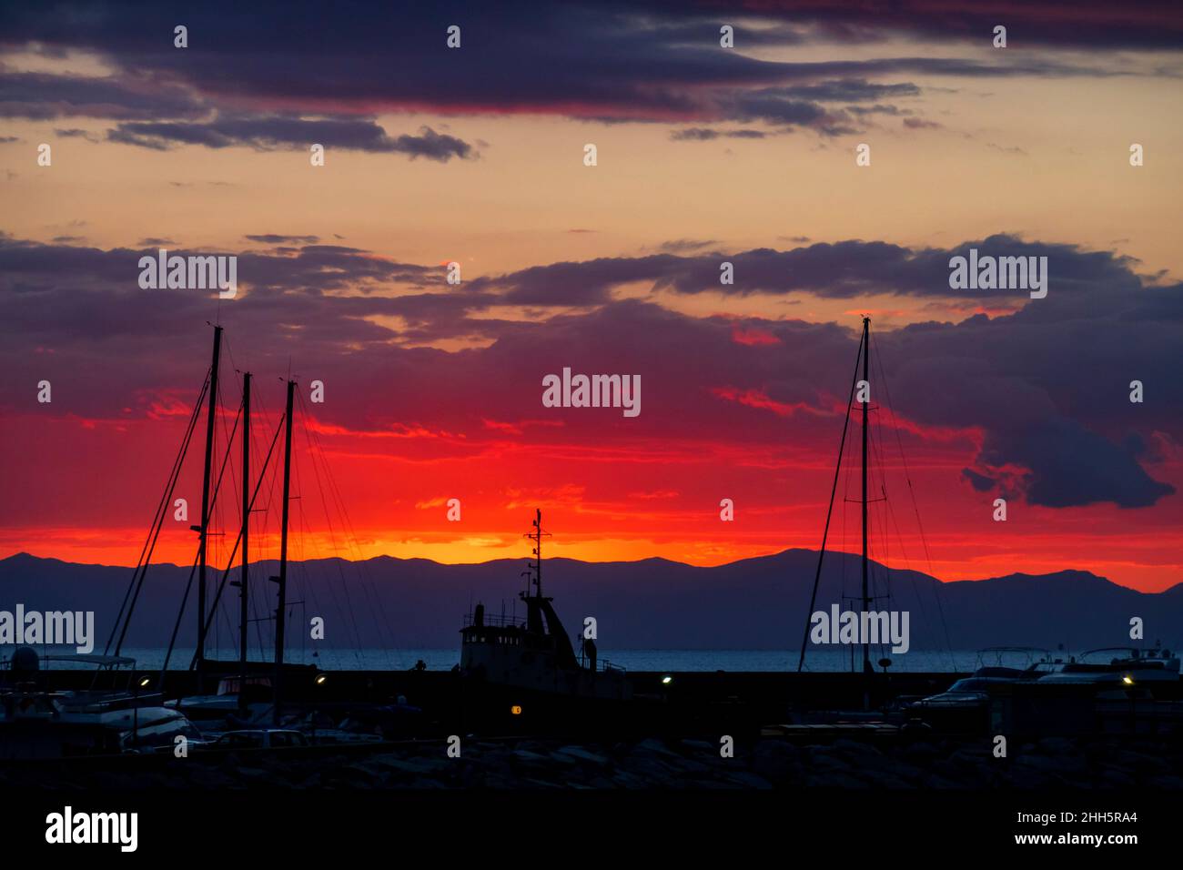 Italie, province de la Sardaigne du Sud, Villasimius, Silhouettes de bateaux amarrés dans le port côtier au coucher de soleil rouge moody Banque D'Images