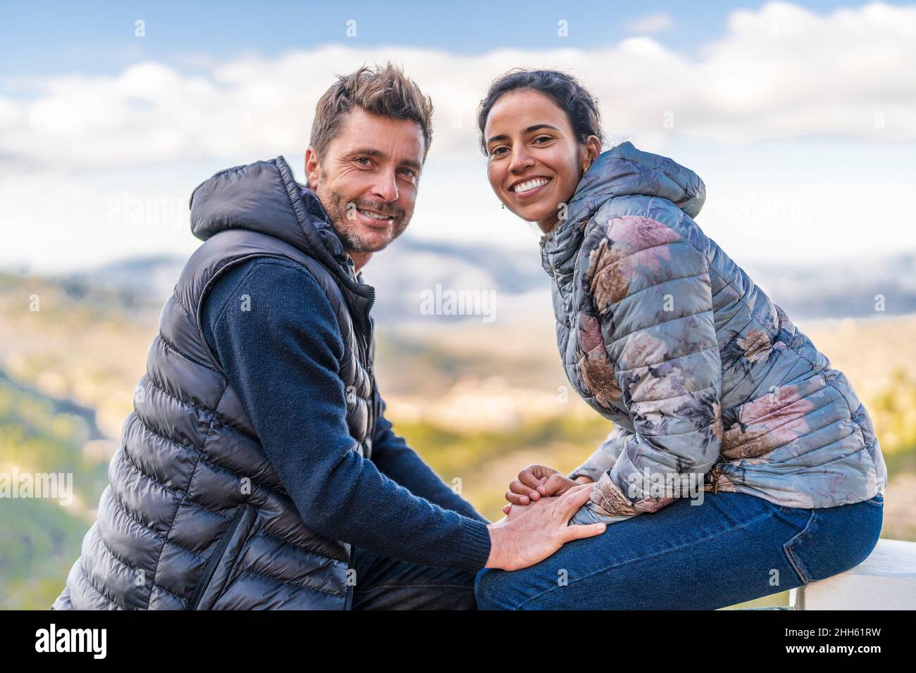 Couple souriant portant une veste matelassée assise au parc Banque D'Images