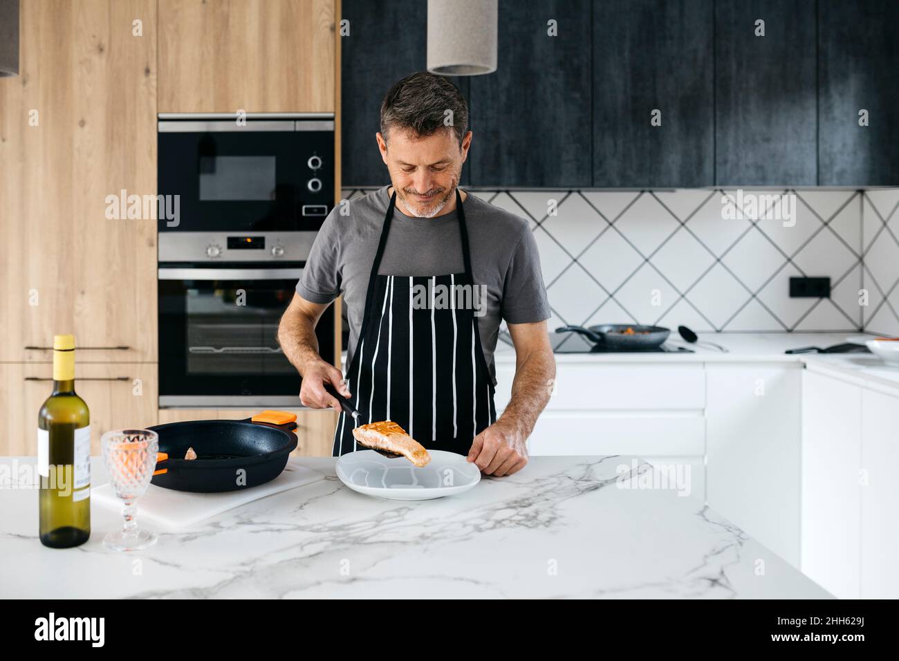 Homme mettant du poisson cuit dans l'assiette sur l'île de cuisine à la maison Banque D'Images