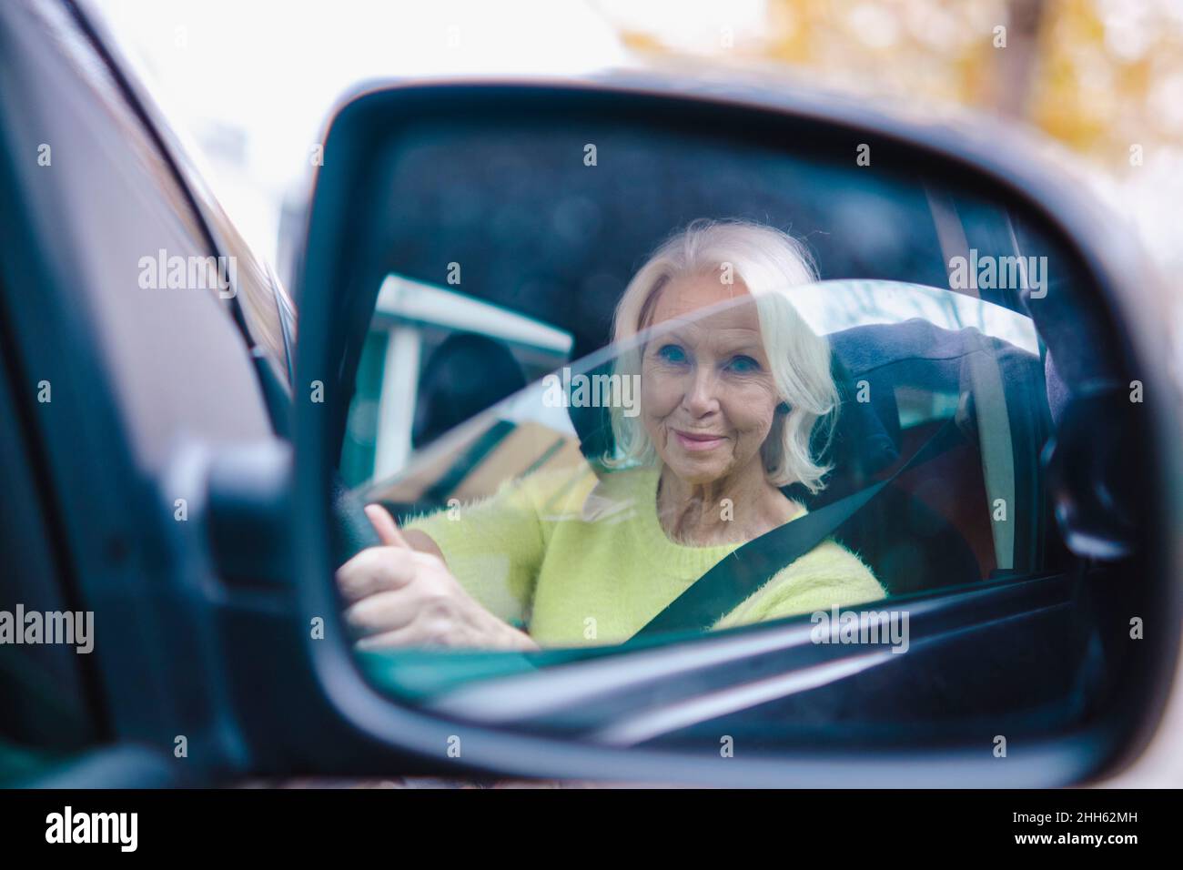 Femme âgée à la retraite conduisant une voiture qui réfléchit sur le rétroviseur extérieur Banque D'Images
